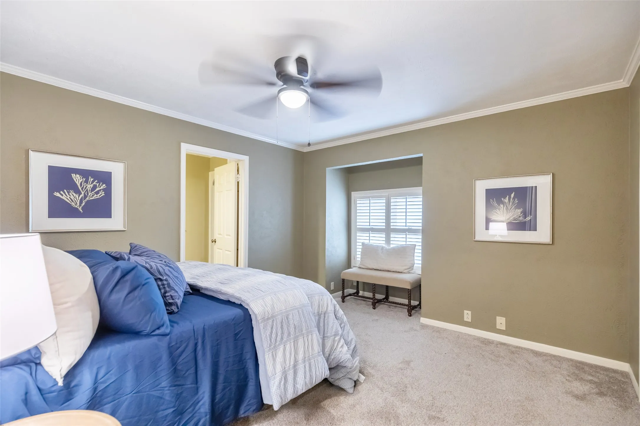 Room featuring a recessed window nook, wall-to-wall carpeting, ceiling fan with integrated lighting, and crown molding