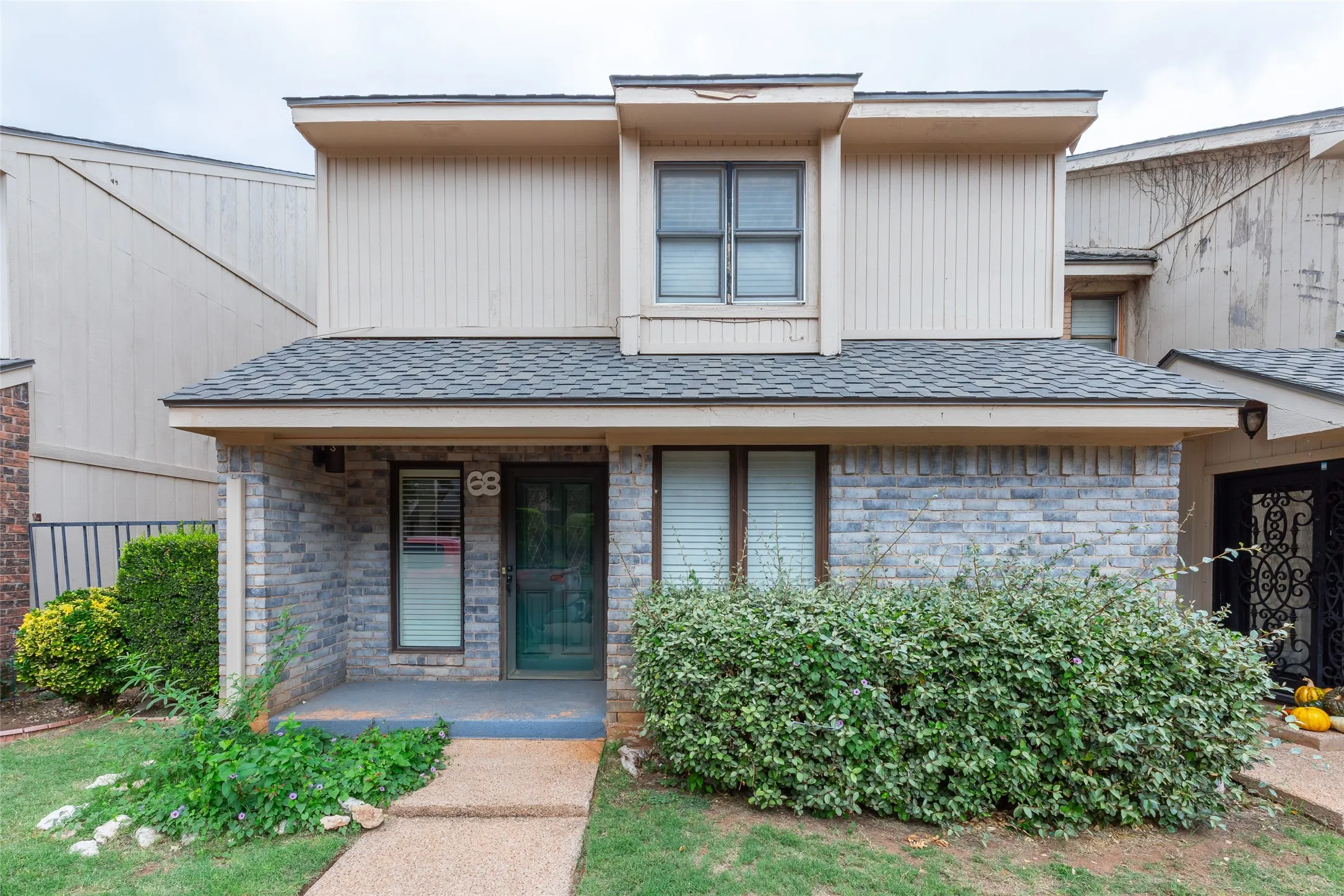 Two-story exterior featuring a brick facade, vertical siding, asphalt shingle roofing, and a concrete front walkway