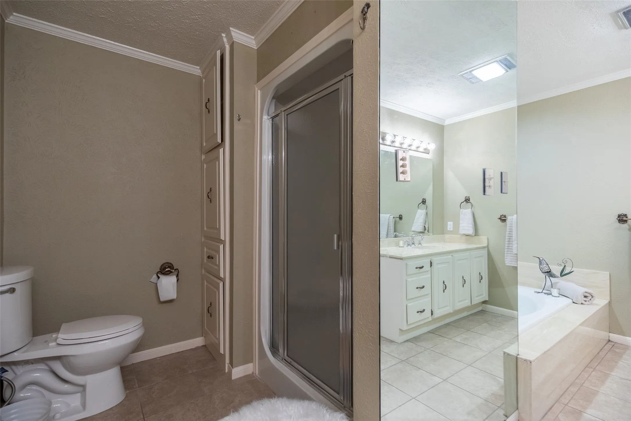 Bathroom featuring a glass-enclosed shower stall, built-in floor-to-ceiling cabinetry, a vanity with drawers, a separate soaking tub, and tile flooring