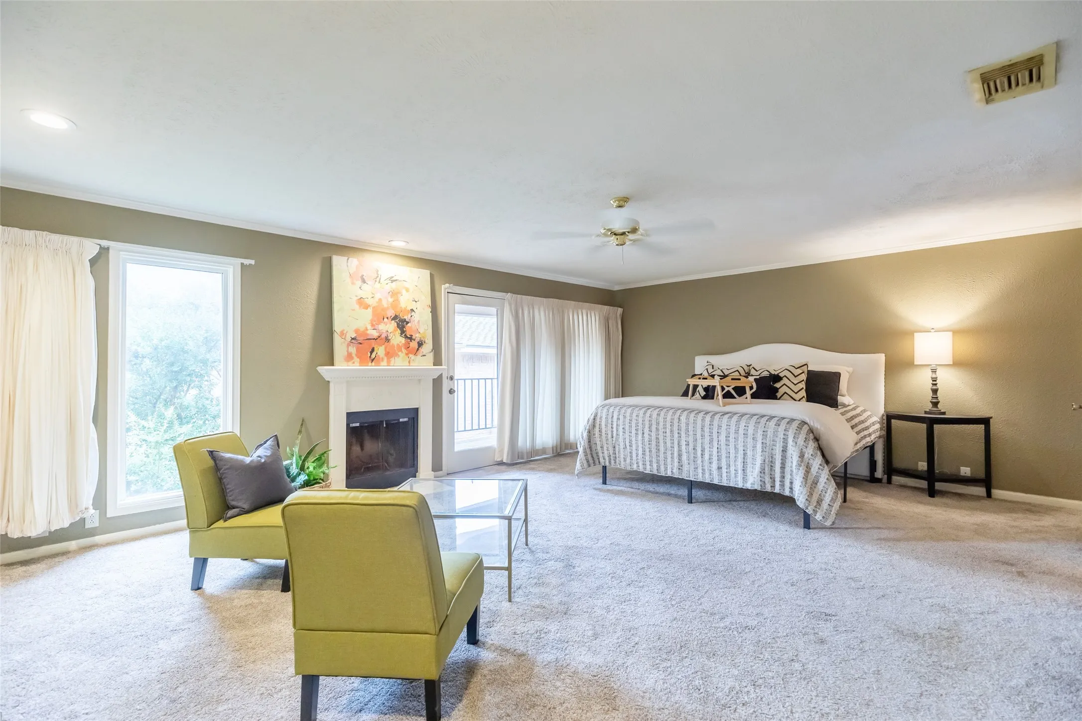 Fireplace with a classic white mantel, full-height windows, wall-to-wall carpeting, ceiling fan, and access to an exterior balcony