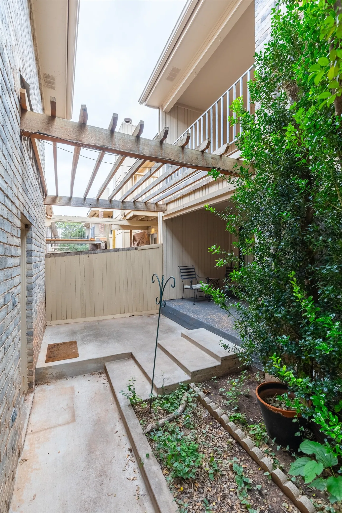 Exterior courtyard featuring a wood pergola, concrete patio, multi-level stairs, privacy fencing, and a stone-edged planter