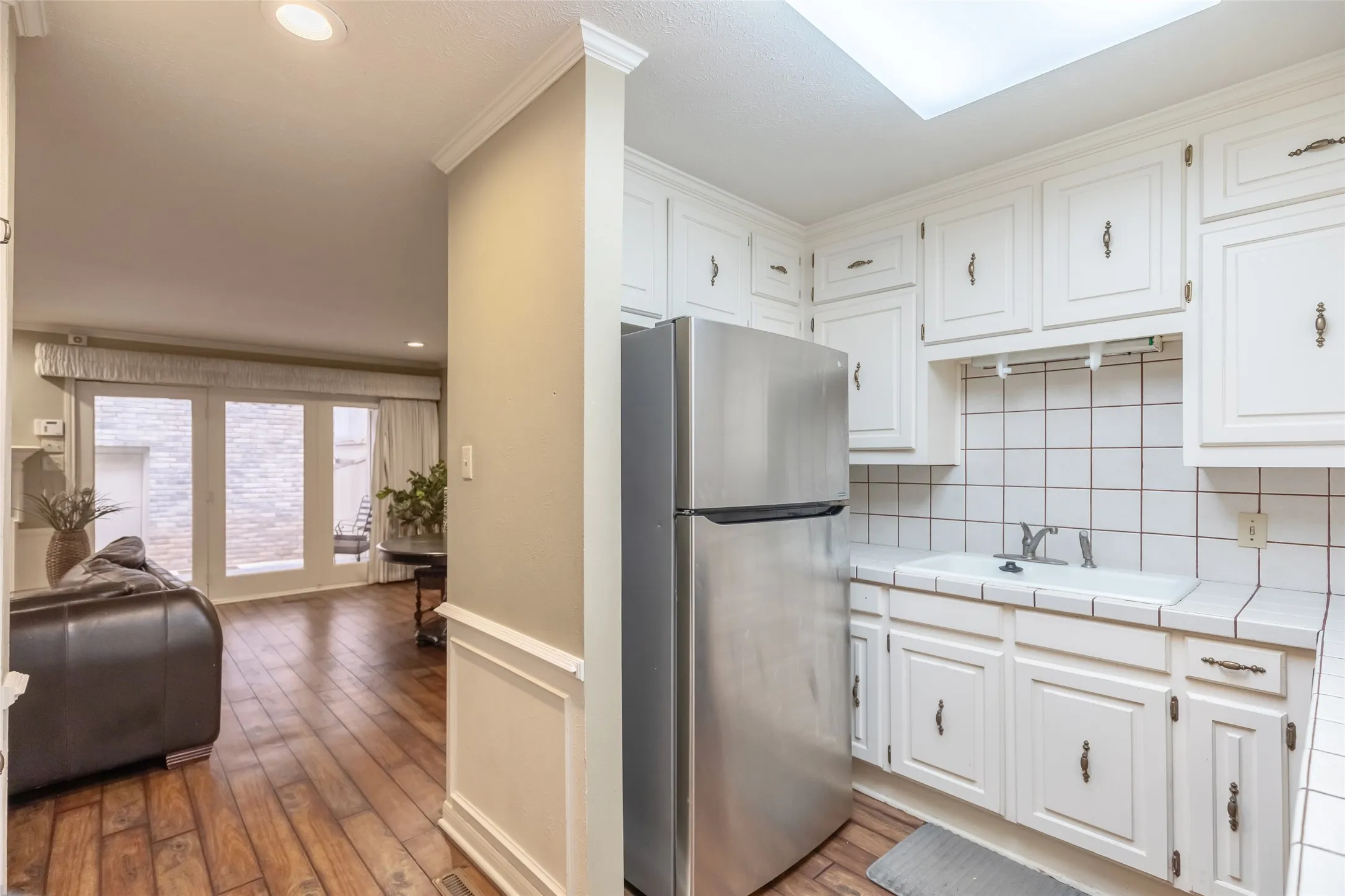 Kitchen featuring white cabinetry, stainless steel refrigerator, tiled countertops, and wood-finish flooring, complemented by a skylight and crown molding
