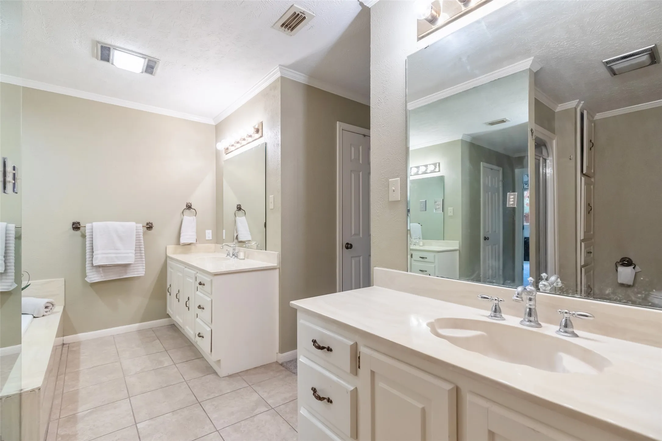 Dual white vanities with integrated sinks, neutral solid-surface countertops, large wall-mounted mirrors, and ceramic tile flooring