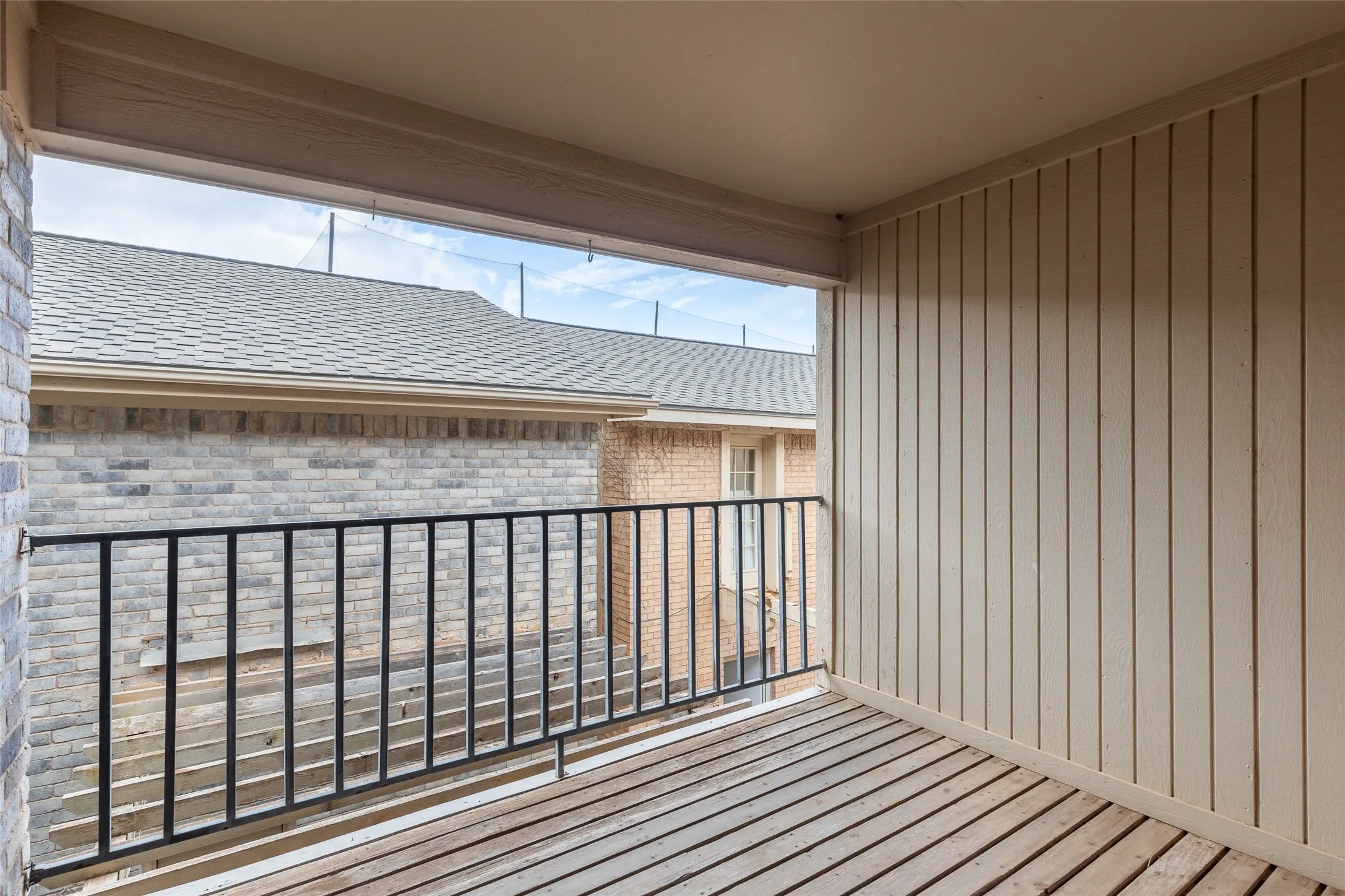 Covered balcony featuring wood-slat flooring, vertical wood siding, and a black metal railing