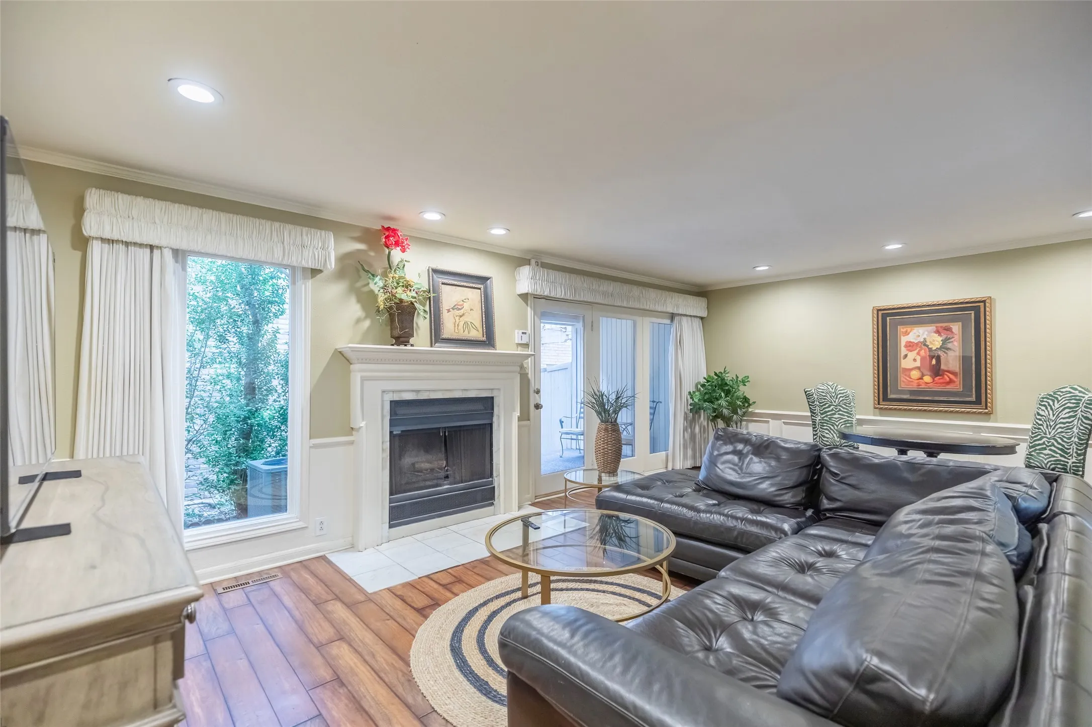 Fireplace with a mantel and tile hearth, wood-finish flooring, recessed lighting, double glass-paneled doors, and wainscoting