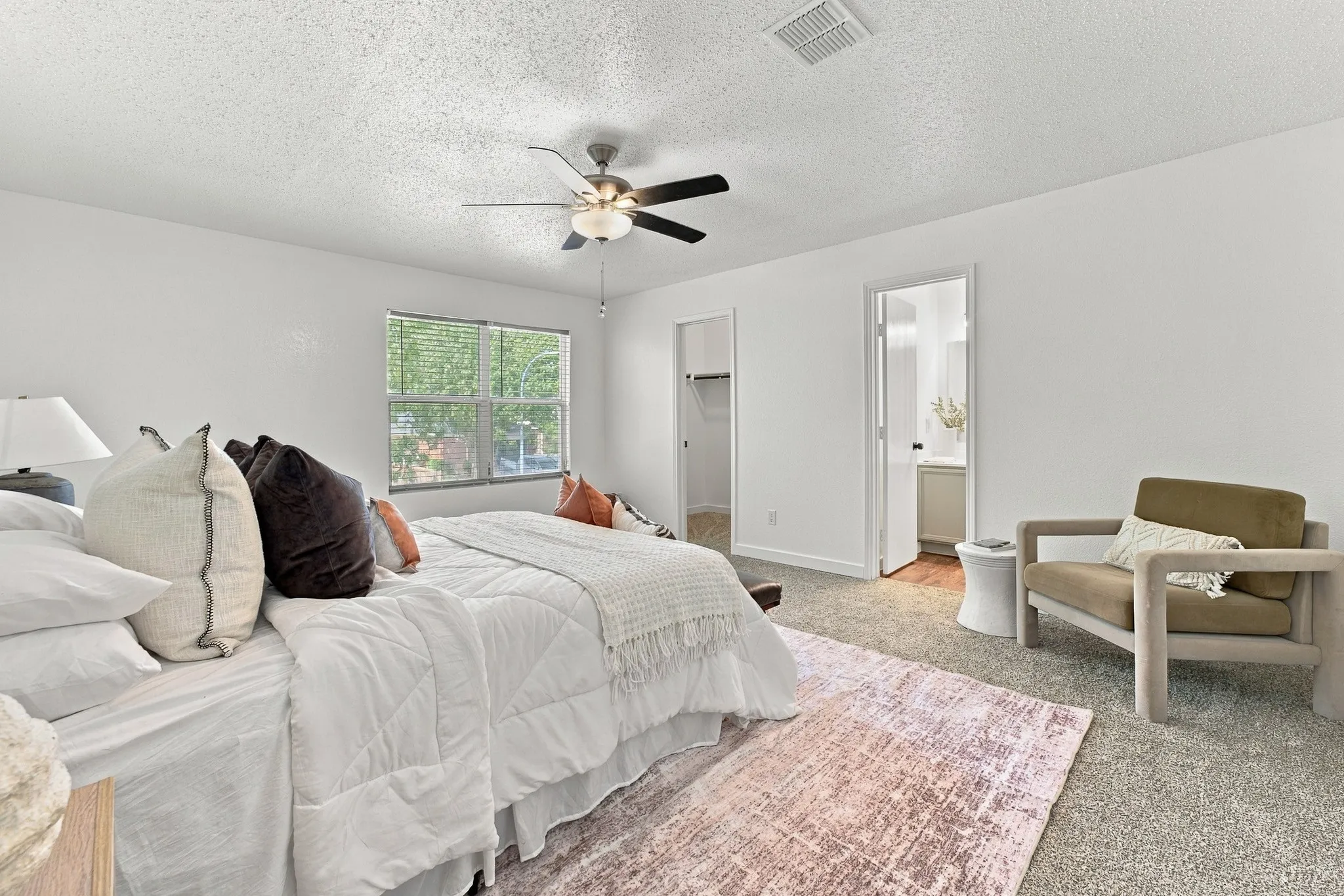 Bedroom featuring neutral carpeting, a multi-blade ceiling fan with integrated lighting, and a walk-in closet