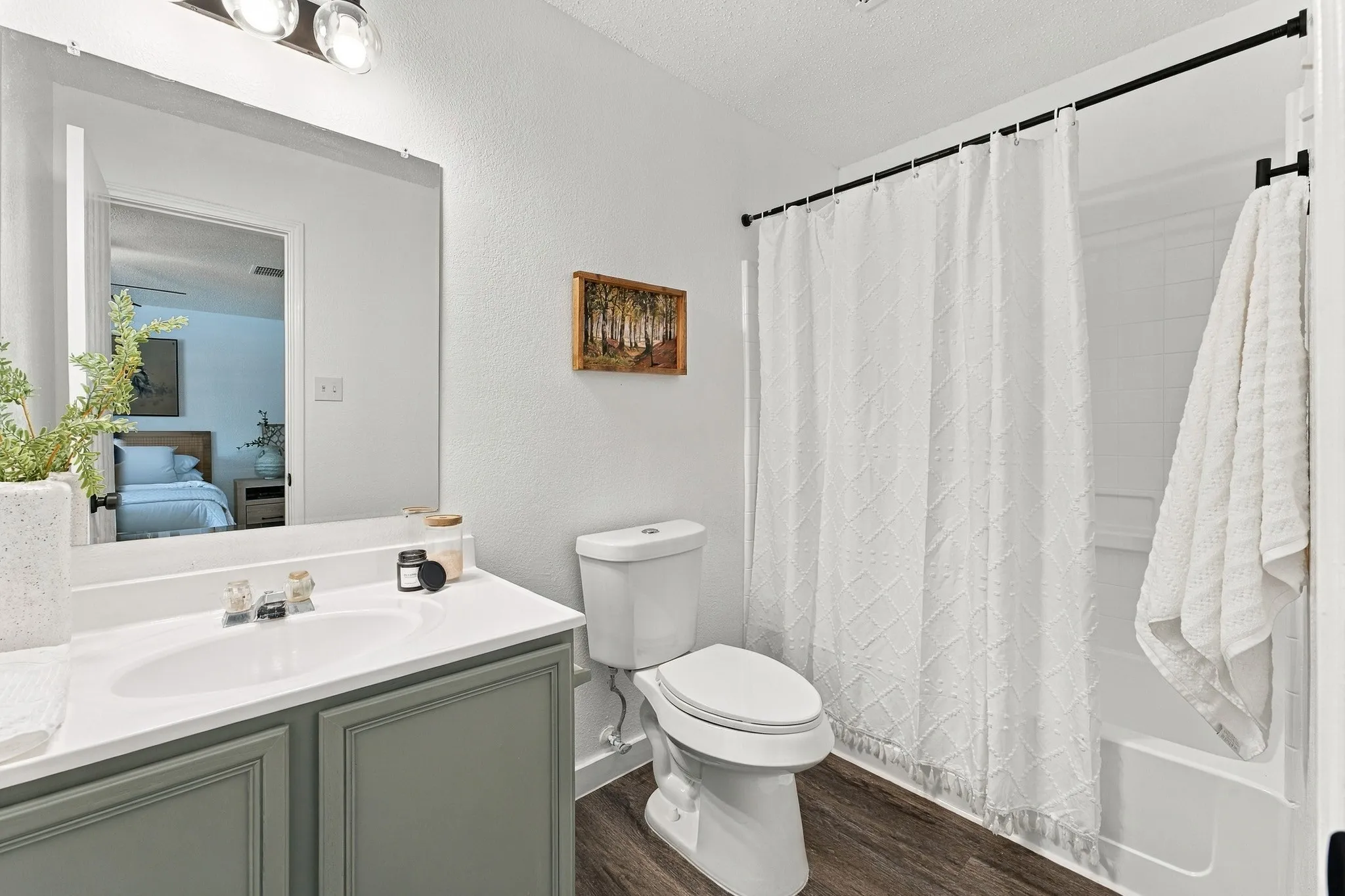 Bathroom featuring a vanity with a solid surface countertop, an integrated sink, a large wall-mounted mirror, wood-finish flooring, and a shower-tub combination with a wall surround