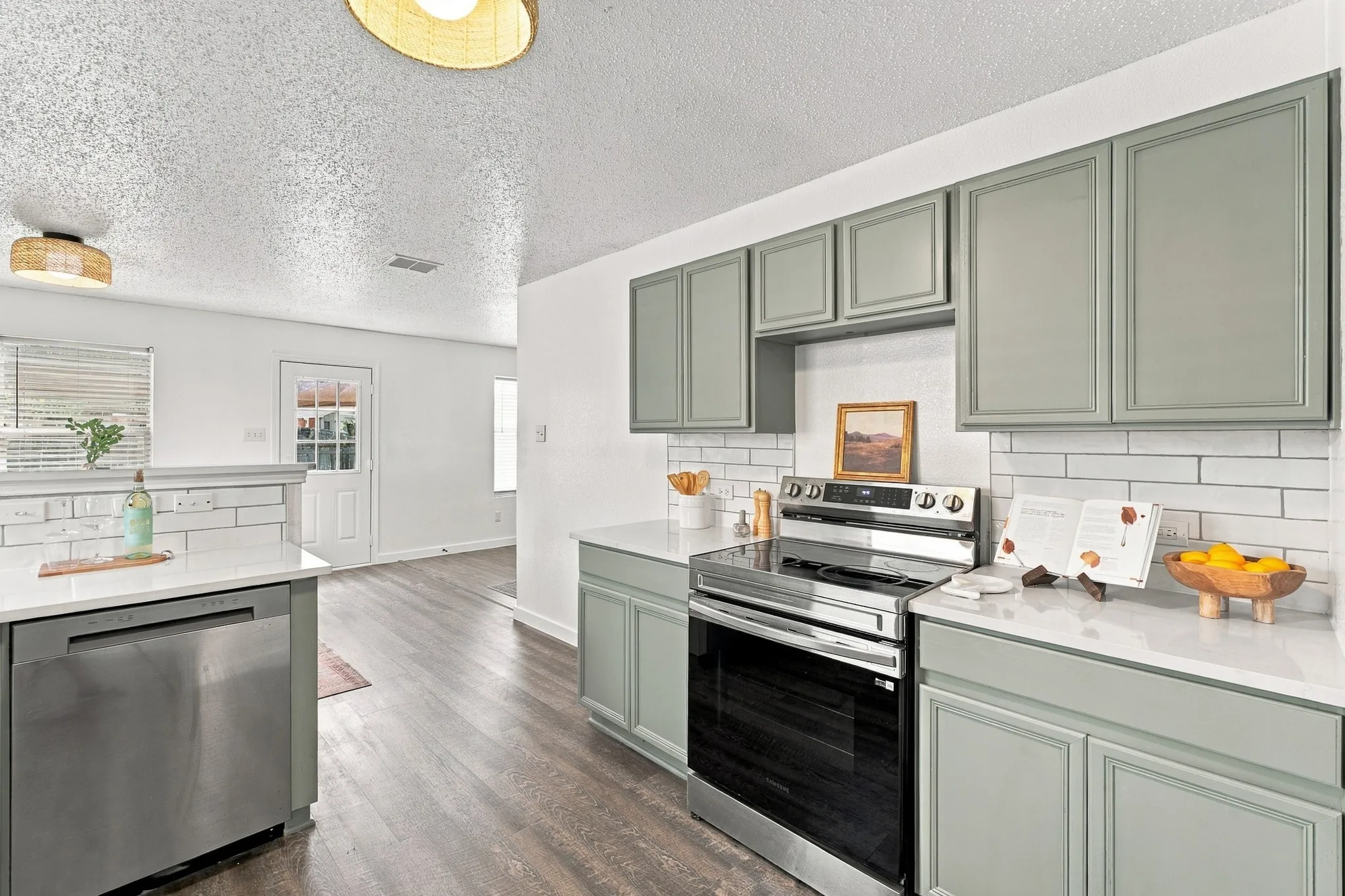 Kitchen featuring sage green shaker-style cabinetry, white quartz countertops, subway tile backsplash, stainless steel appliances, and wood-finish flooring