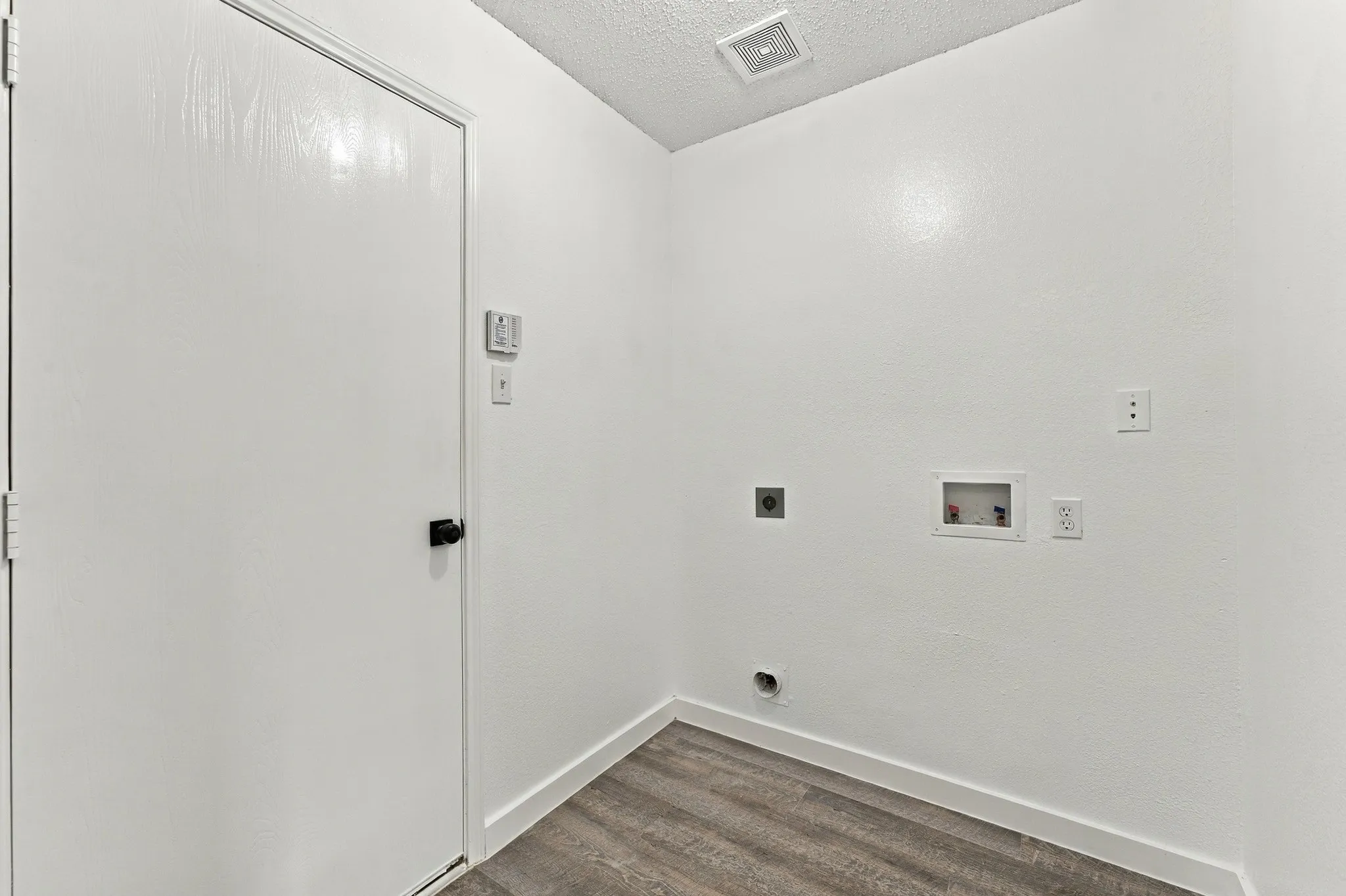 Dedicated utility space featuring wood-finish flooring, white walls, and a recessed plumbing connection box with electrical outlets