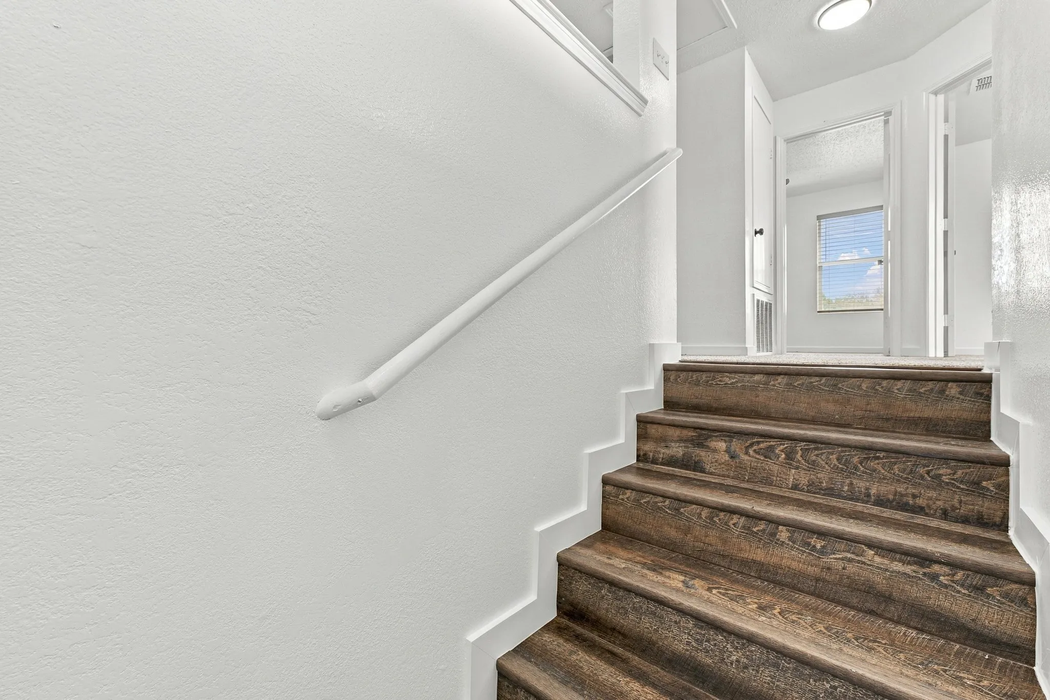Staircase featuring wood-finish treads, white painted walls, and a matching handrail