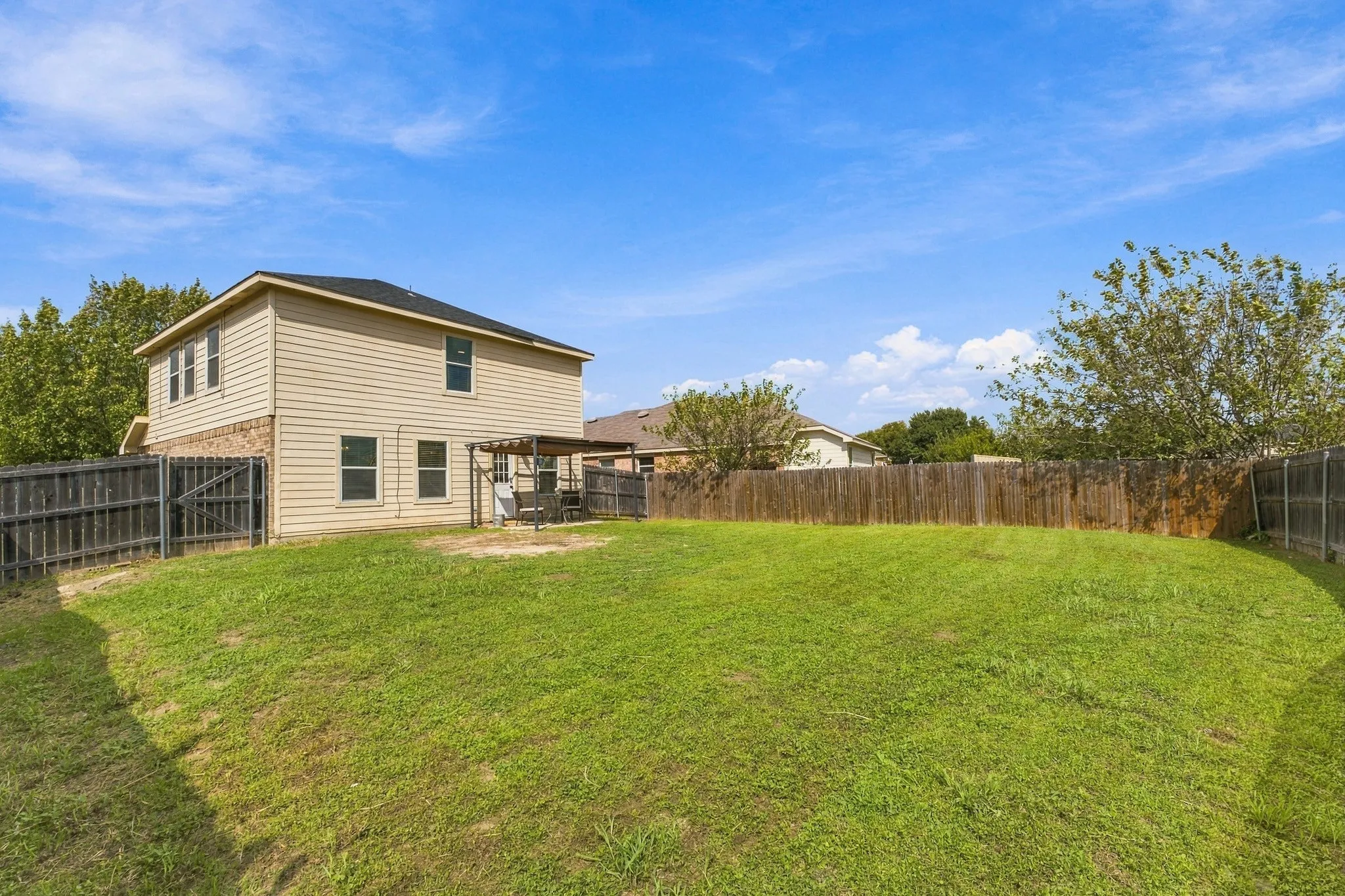 Expansive backyard featuring a sodded lawn, wood privacy fencing, and a pergola-covered patio