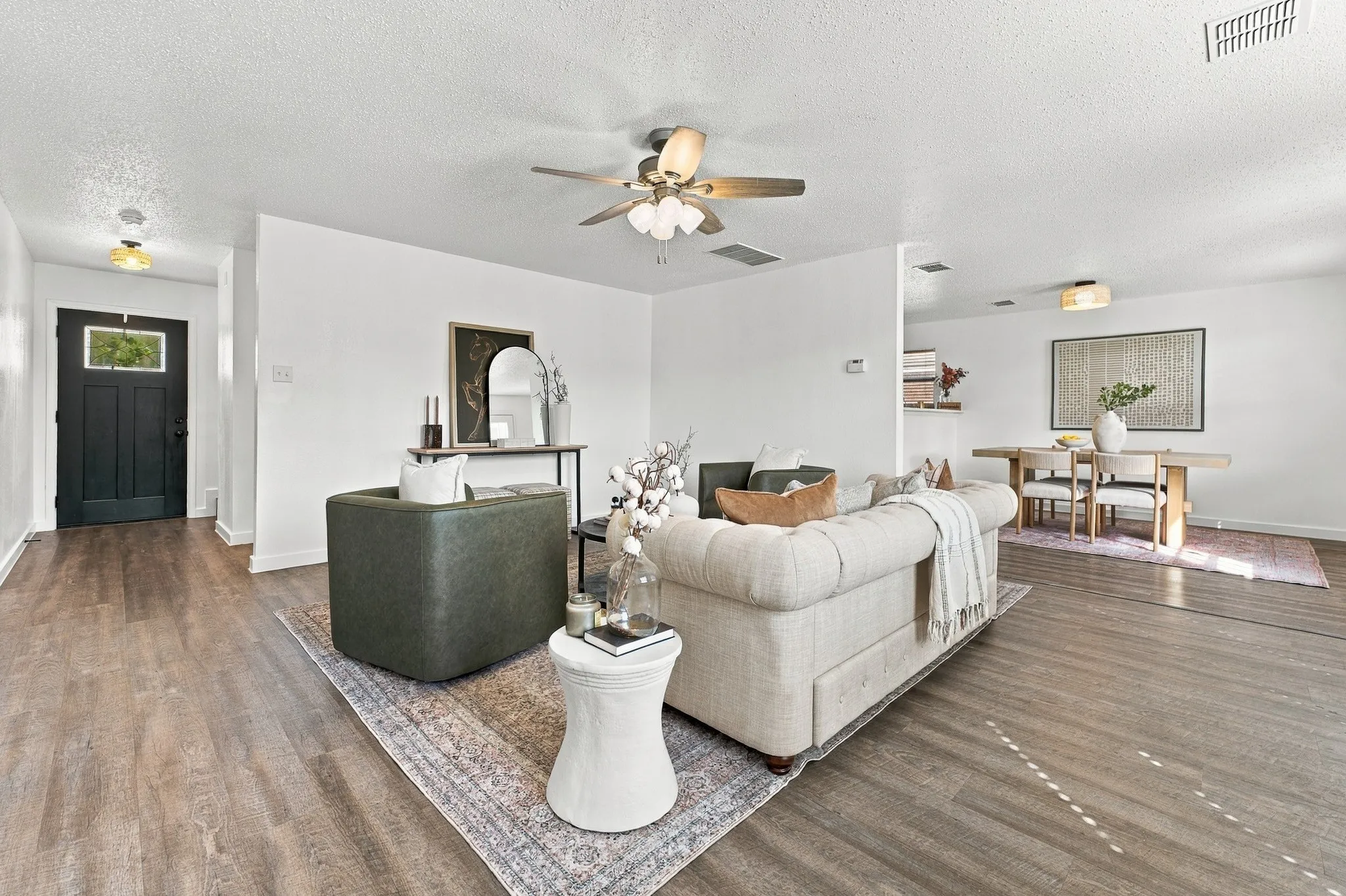 Living area featuring wood-finish flooring, a ceiling fan with integrated lighting, and a black front door with a glass inlay
