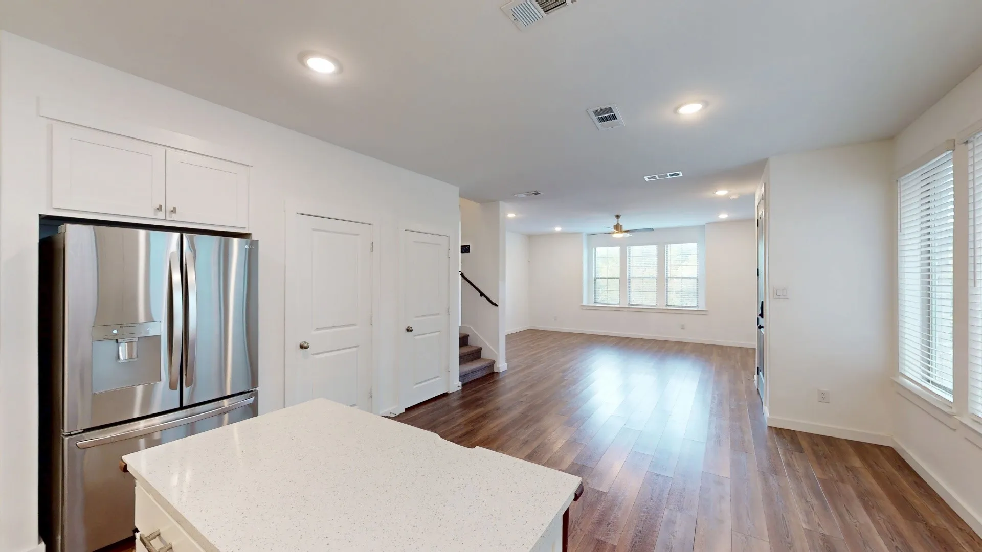 Kitchen featuring an island with a light-toned quartz countertop, stainless steel refrigerator, white cabinetry, wood-finish flooring, and recessed lighting