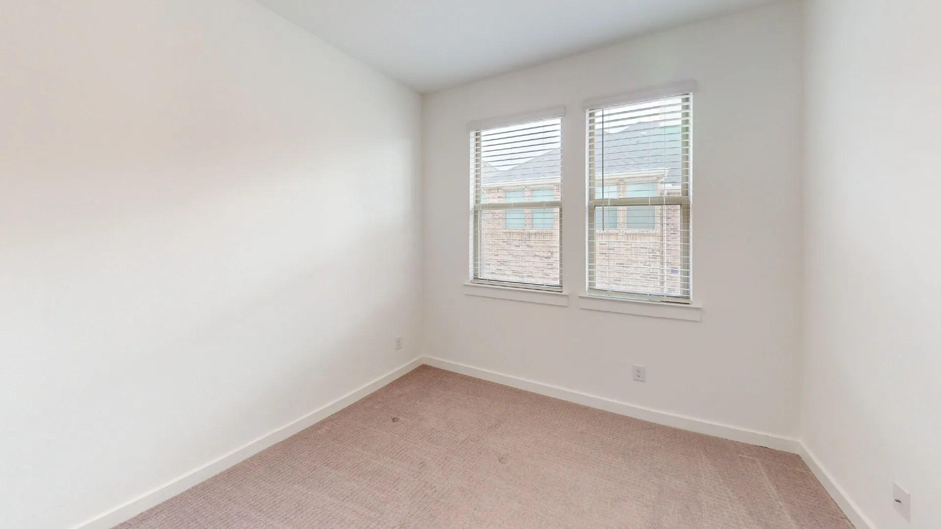 Neutral-toned carpeted flooring, white walls, and dual windows equipped with horizontal blinds