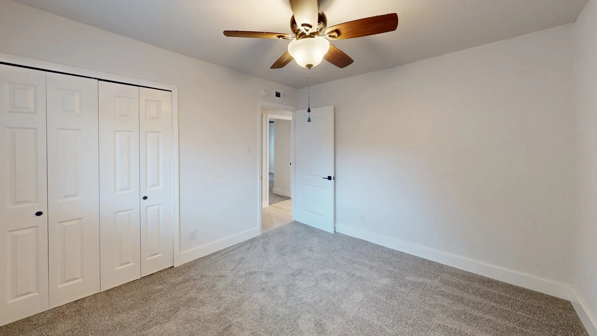 Neutral interior room featuring neutral carpeting, a ceiling fan with integrated lighting, and white bi-fold closet doors