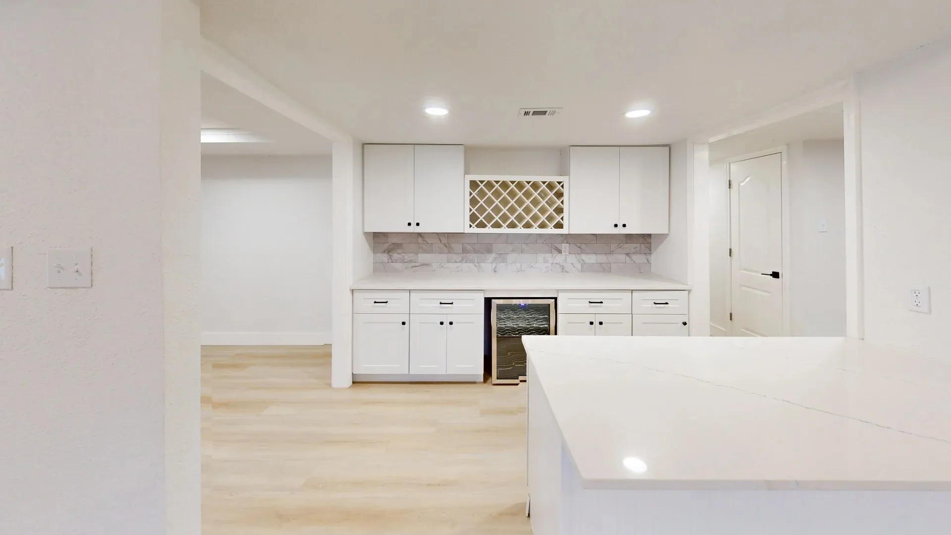 White shaker-style cabinetry, integrated wine refrigerator, built-in wine rack, quartz countertop, and patterned stone-finish backsplash