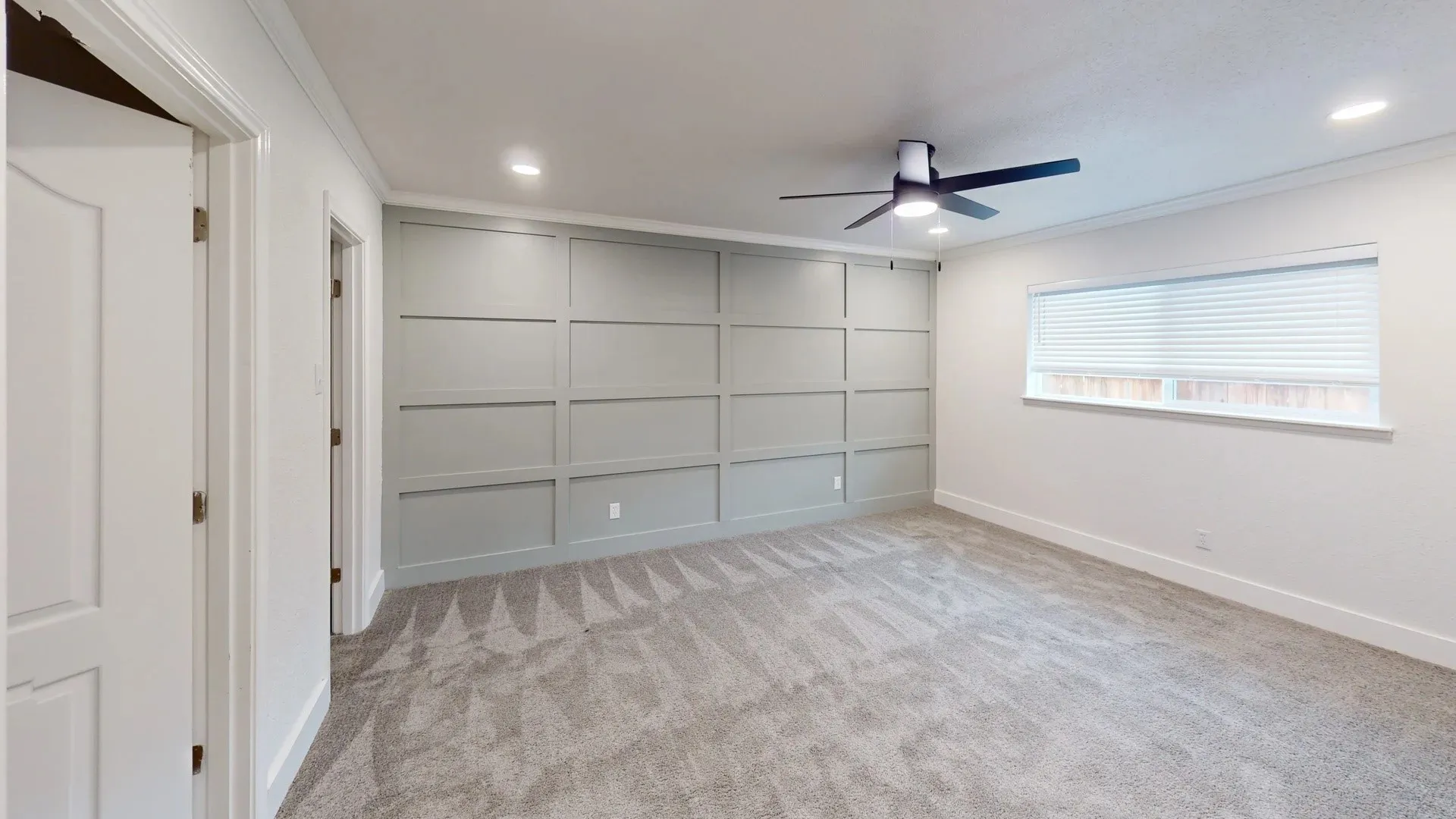 Grey-painted wainscoting accent wall, recessed lighting, ceiling fan with integrated lighting, neutral wall-to-wall carpeting, and horizontal window blinds