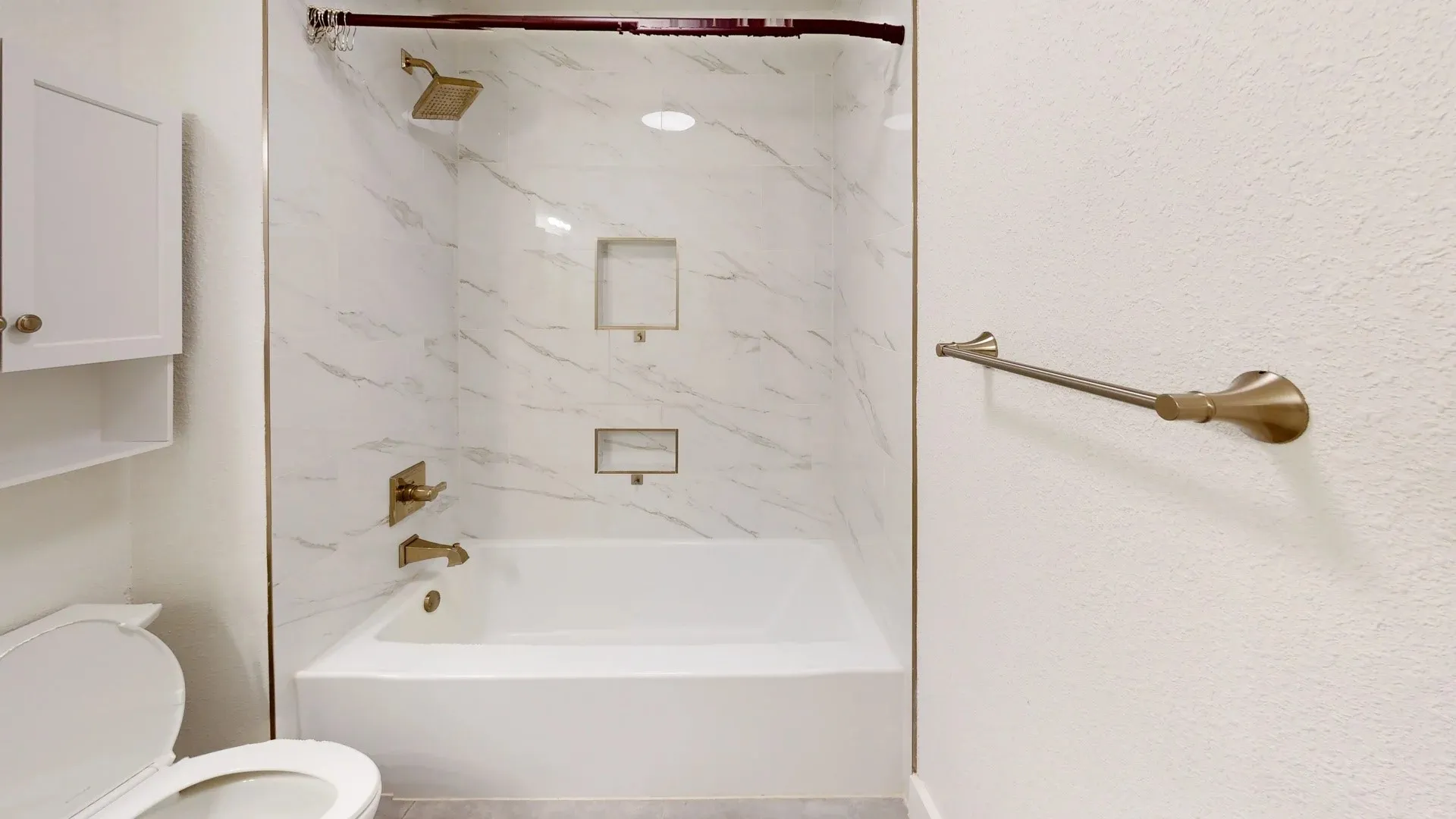 Bathtub and shower combination featuring stone-finish wall surround, dual built-in recessed niches, and metallic-finish hardware