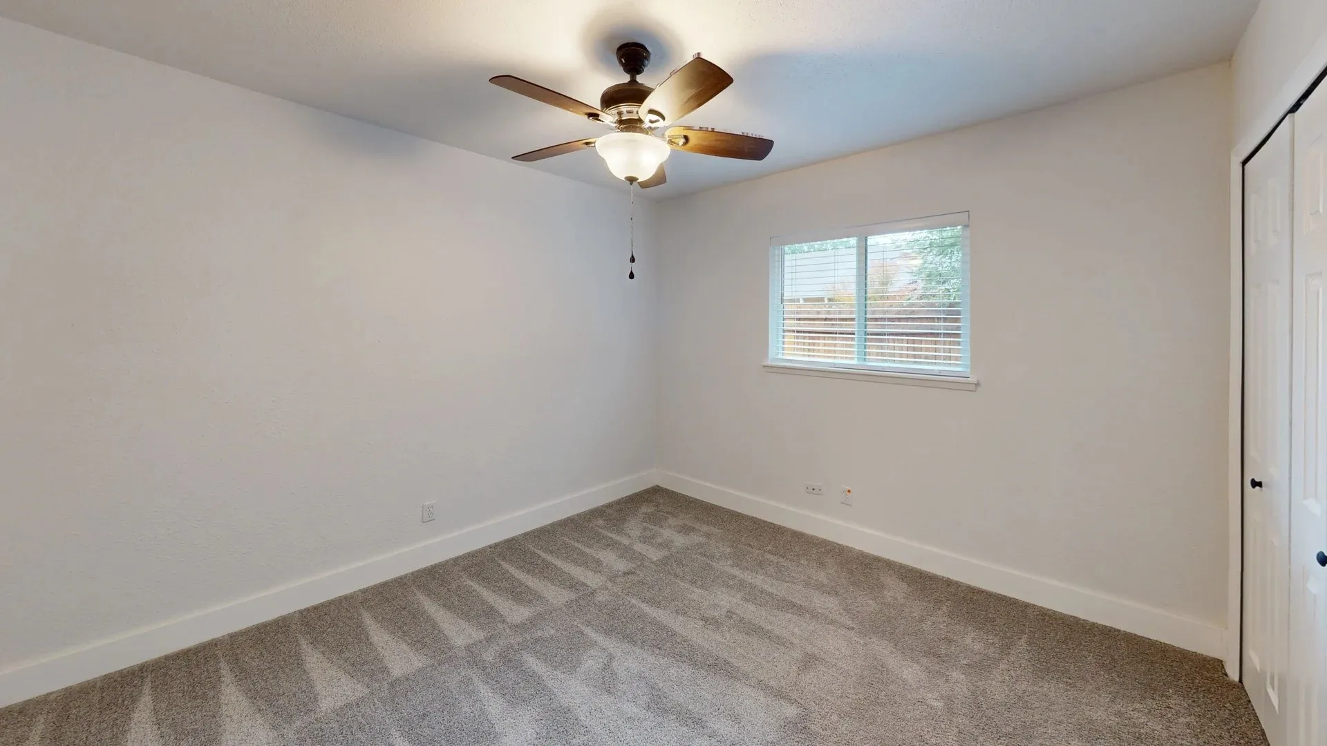 Neutral-toned wall-to-wall carpeting, ceiling fan with integrated light fixture, dual-panel closet doors, and sliding window