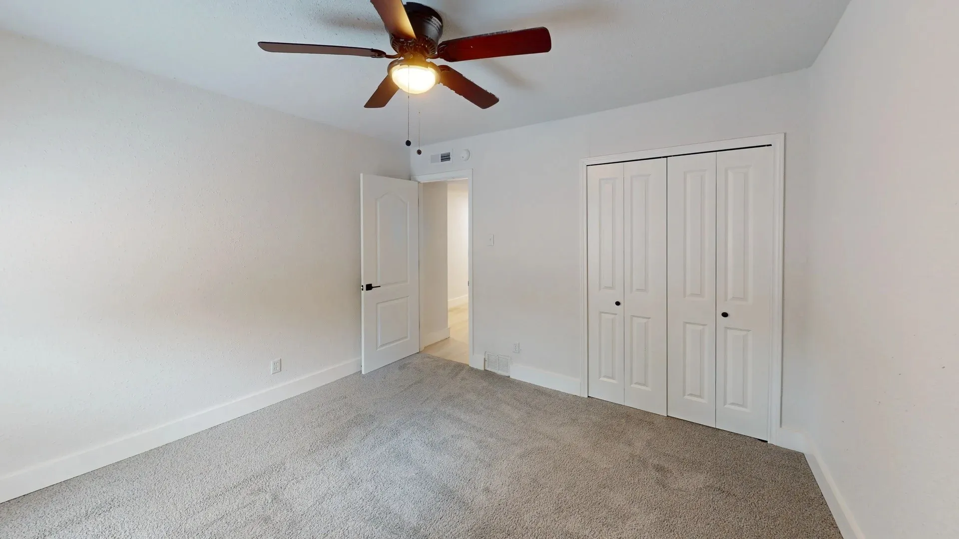 Room featuring neutral carpeting, a ceiling-mounted light fixture with a fan, and a double-door closet