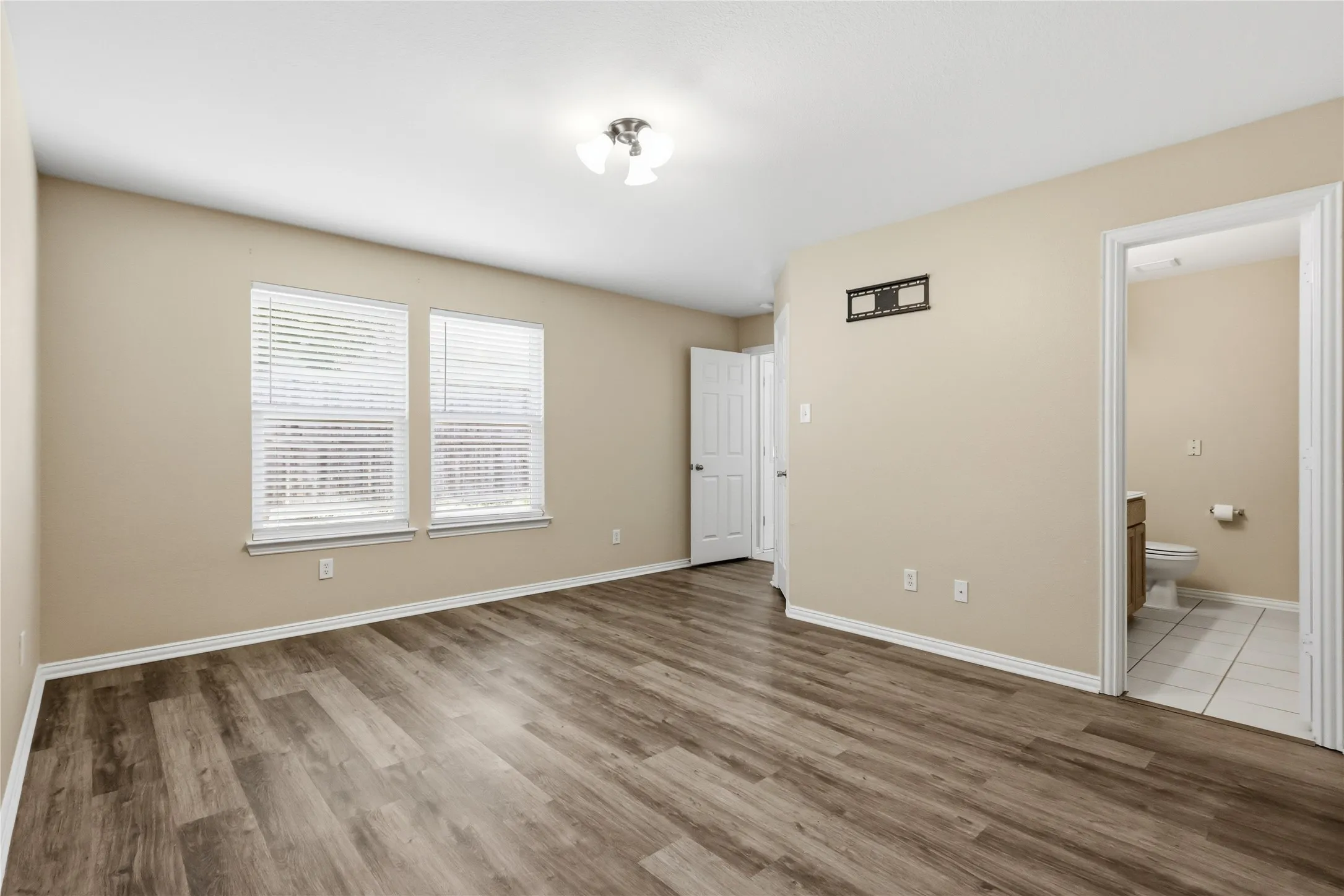 Interior space featuring wood-finish flooring, dual windows with horizontal blinds, neutral wall paint, and a ceiling-mounted light fixture