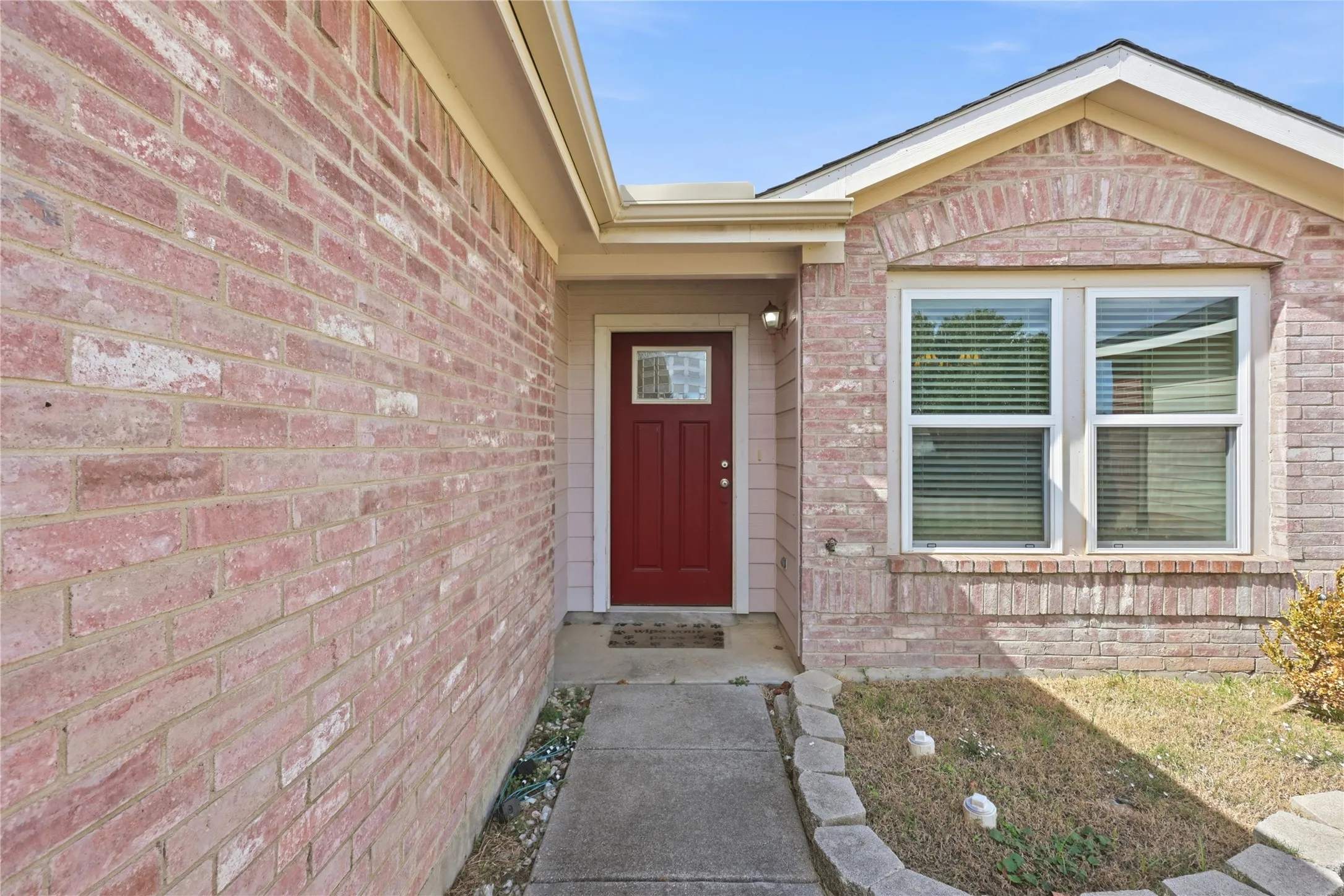 Brick exterior facade featuring a recessed entry, a solid core door with a glass inset, and double-pane windows with arch-topped detailing