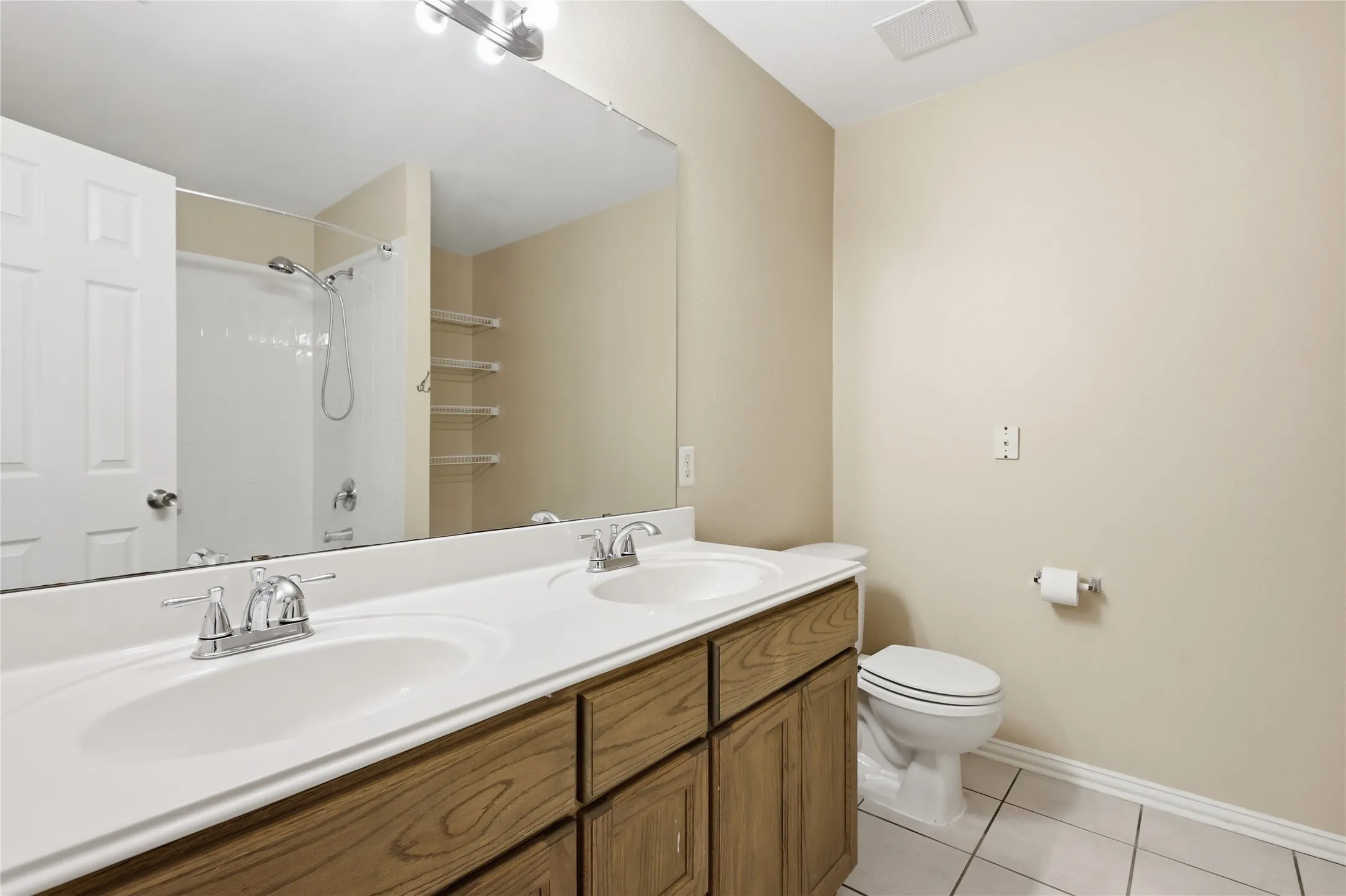 Double-sink vanity with wood-finish cabinetry, integrated countertop, chrome dual-handle faucets, and full-width vanity mirror
