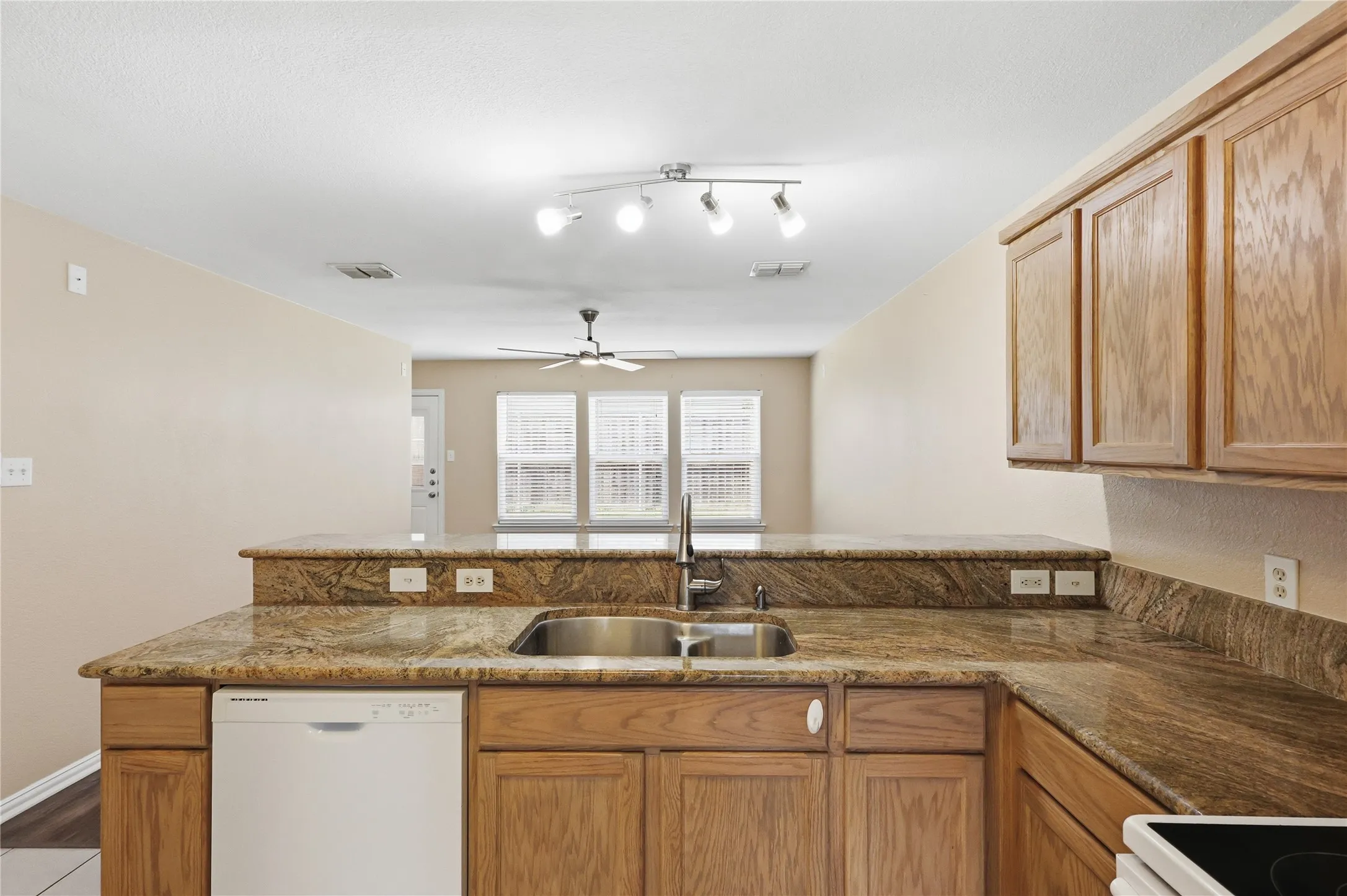 Kitchen featuring natural stone countertops, wood cabinetry, a dual-basin stainless steel sink with a high-arch faucet, and a built-in dishwasher