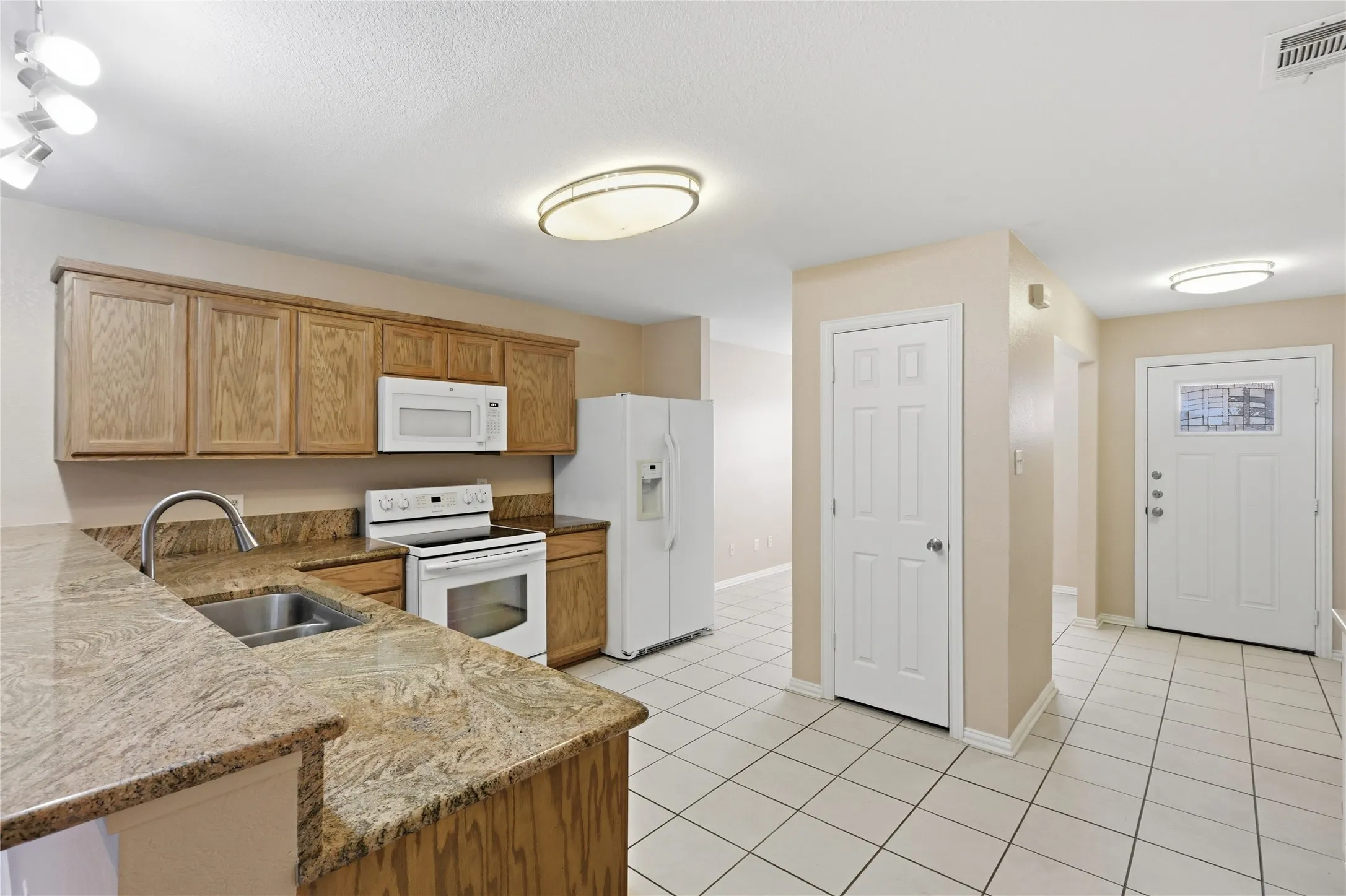 Kitchen featuring wood cabinetry, stone countertops, tiled flooring, an integrated microwave, and an entry door with a decorative glass panel