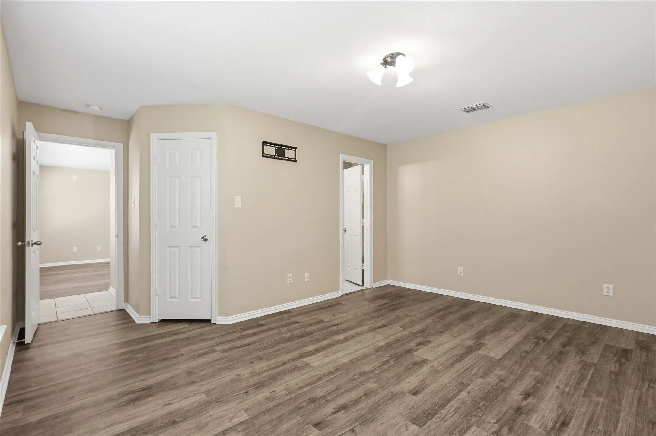Interior room featuring wood-finish flooring, neutral wall tones, multi-panel interior doors, and overhead light fixture