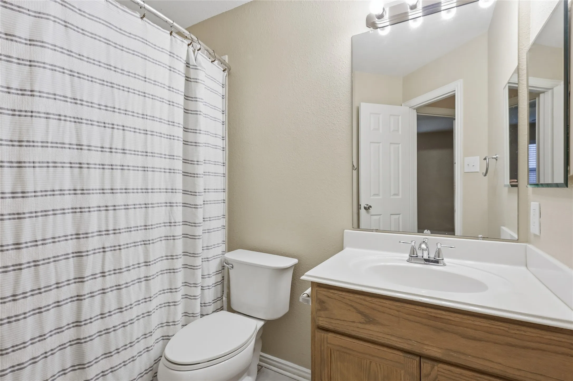 Bathroom featuring a vanity with a white composite countertop, integrated sink, polished chrome faucet, and large wall-mounted mirror with integrated lighting