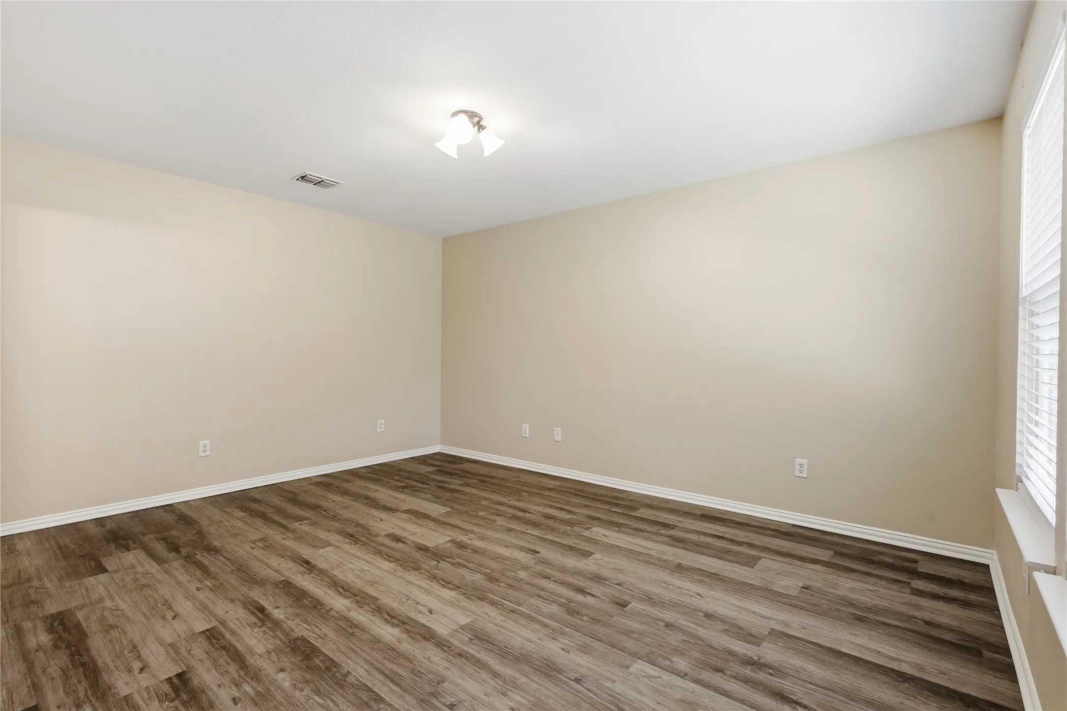 Room featuring wood-finish flooring, neutral wall paint, a flush-mount ceiling light fixture, and horizontal blind window treatments