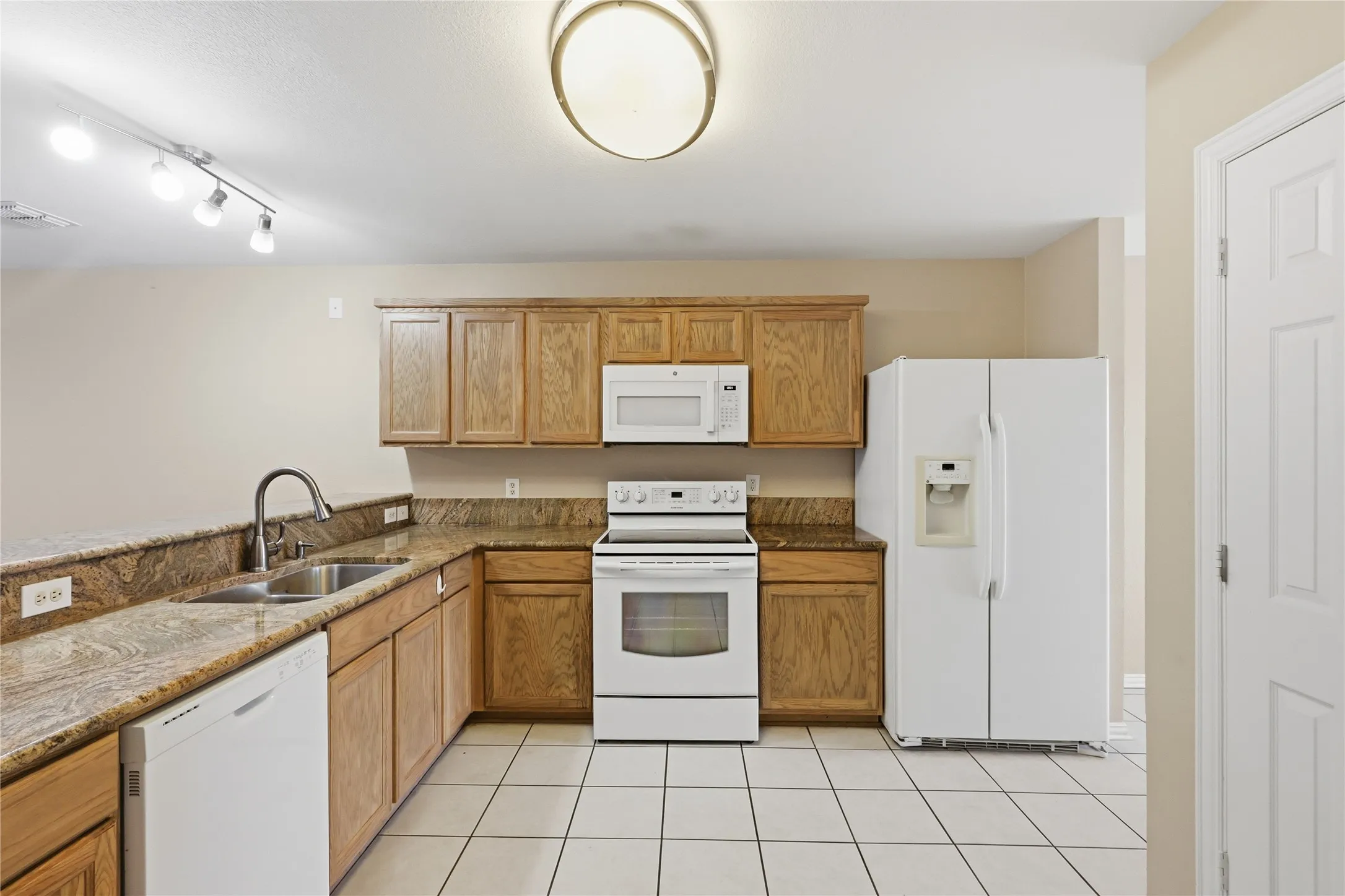 Kitchen featuring wood cabinetry, stone countertops, a stainless steel double-basin sink, tile flooring, and white built-in appliances including an over-the-range microwave