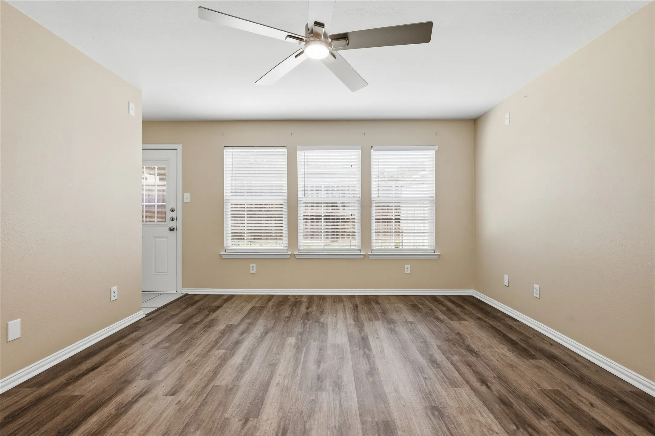Neutral-toned walls featuring wood-finish flooring, a contemporary ceiling fan, and three windows with horizontal blinds