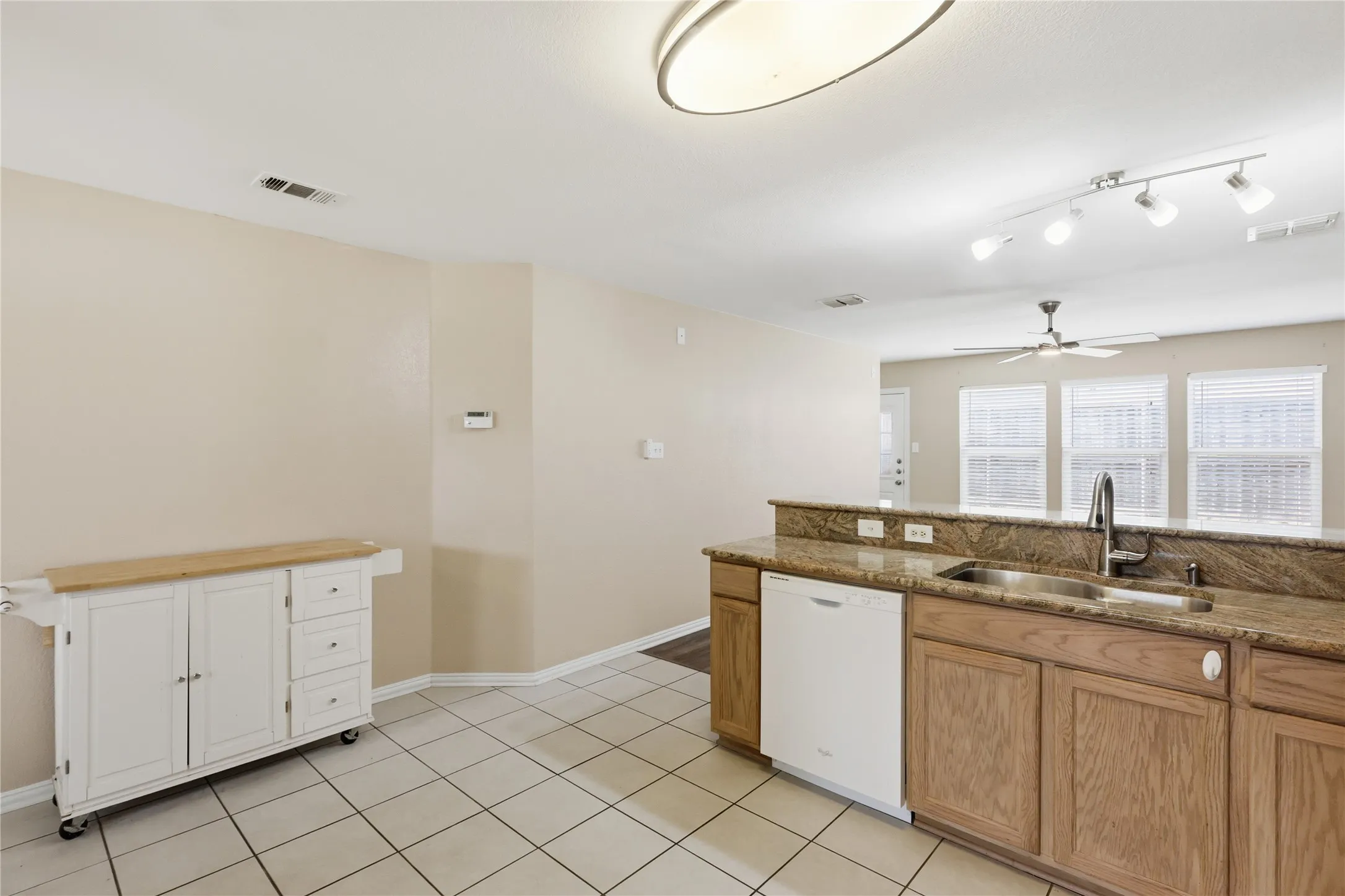 Kitchen featuring stone countertops, integrated stainless steel sink with high-arc faucet, wood-finish cabinetry, and ceramic tile flooring