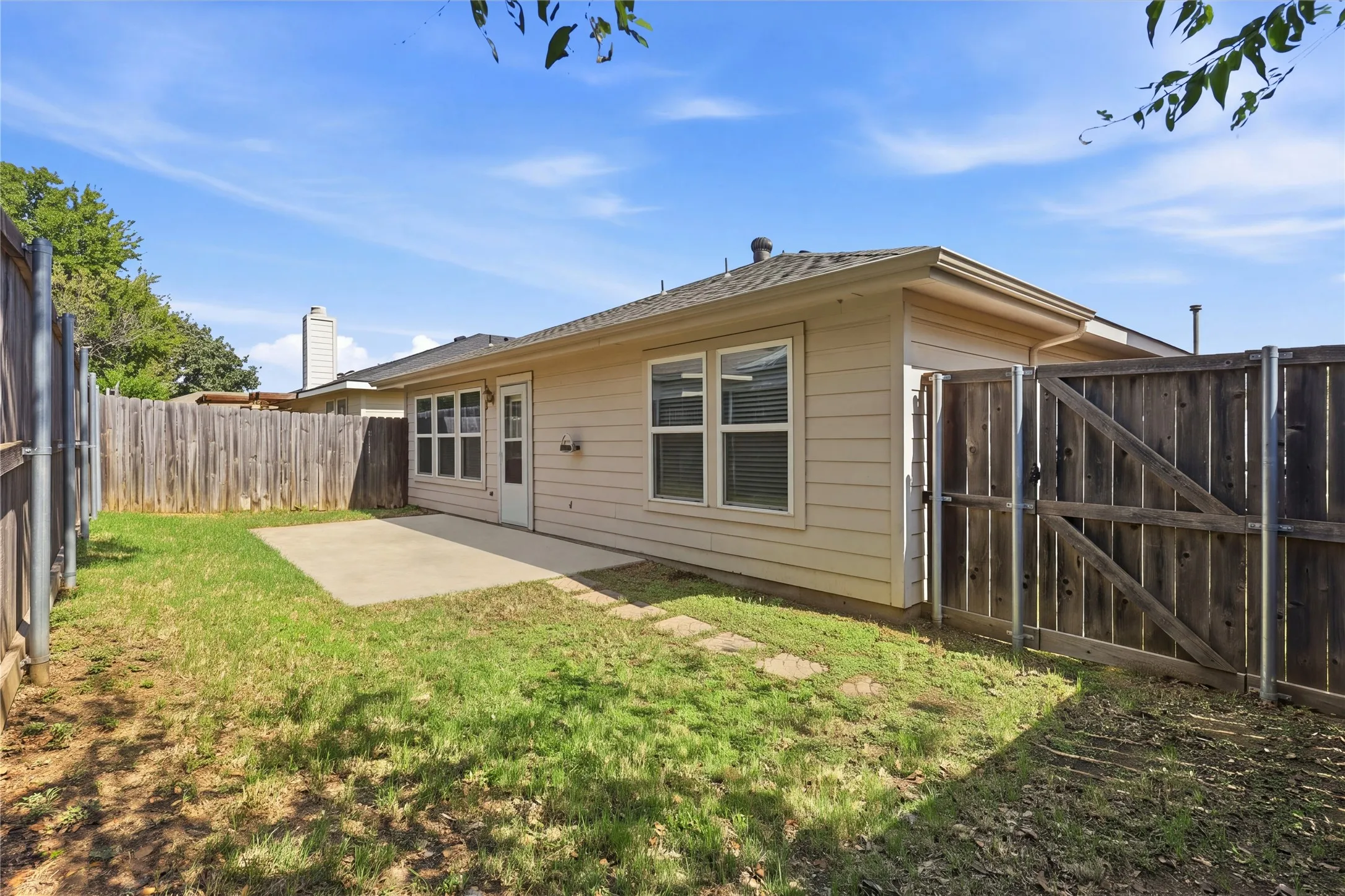 Exterior rear elevation featuring light-colored horizontal siding, a concrete patio, and a fully enclosed wood privacy fence