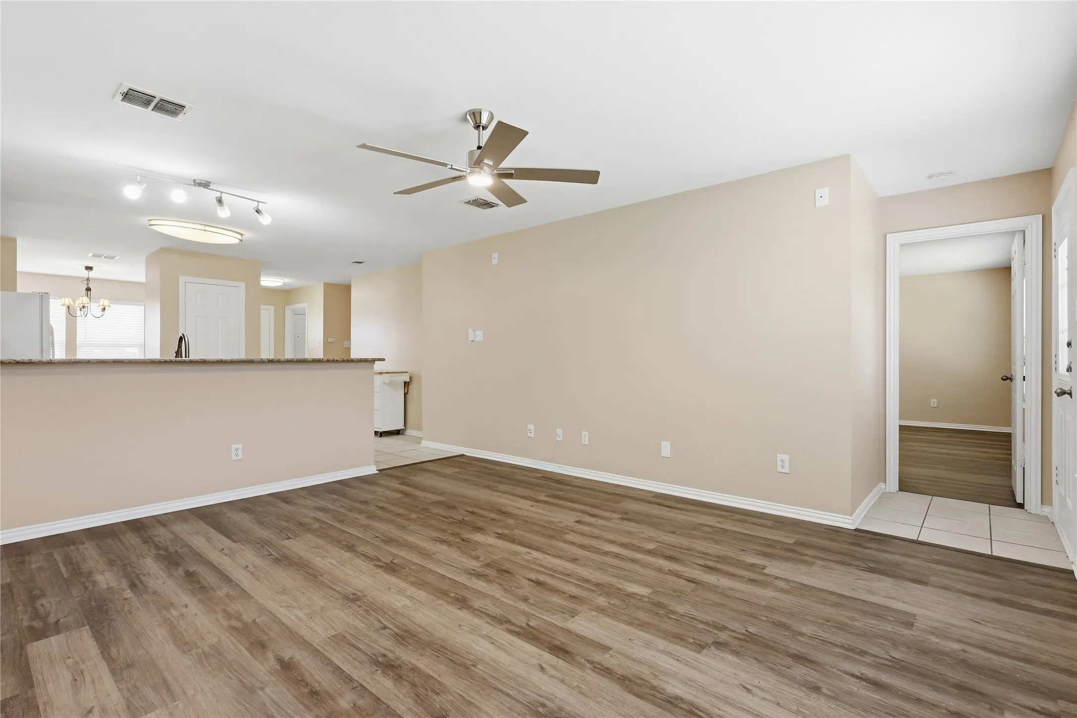 Living area featuring wood-finish flooring, a ceiling fan with integrated lighting, a stone-surfaced breakfast bar, and multi-directional track lighting