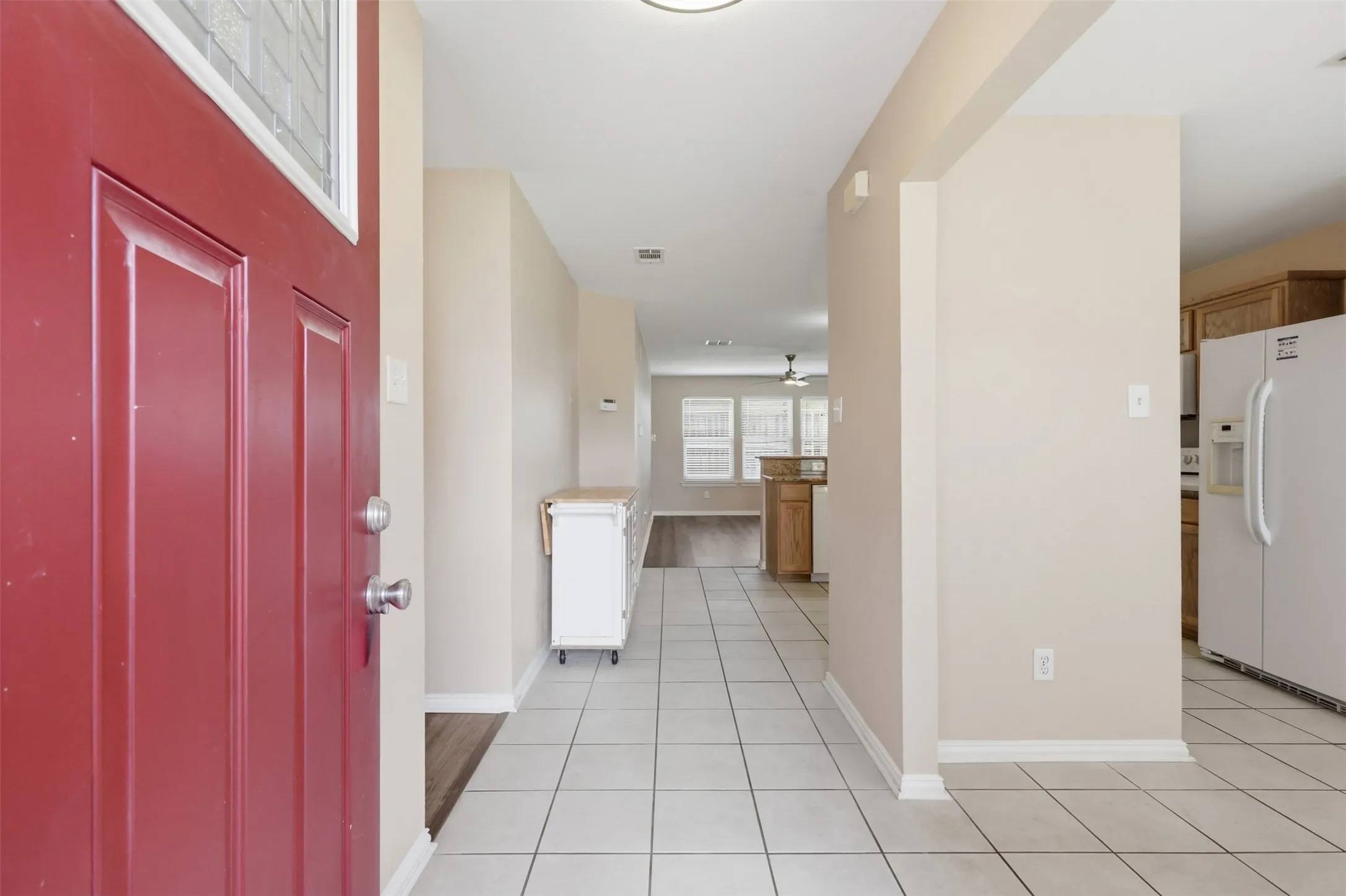 Entryway featuring a bold red paneled door with glass inlay and neutral ceramic tile flooring throughout