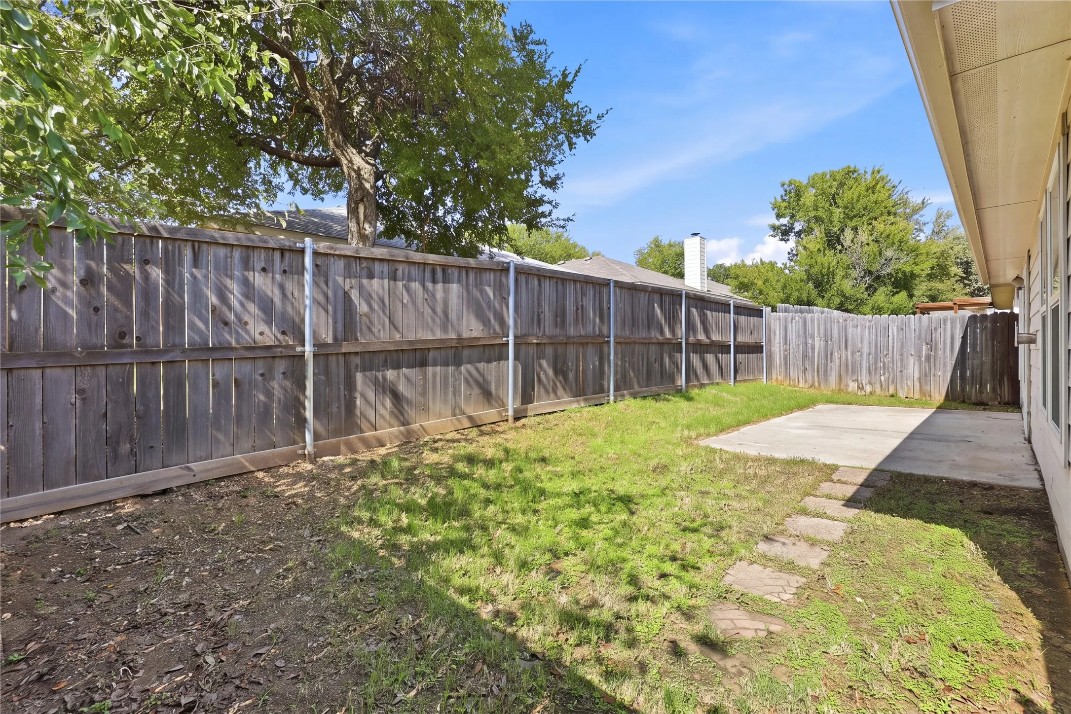 Backyard featuring a concrete patio, stepping stone path, wood fencing, and mature trees