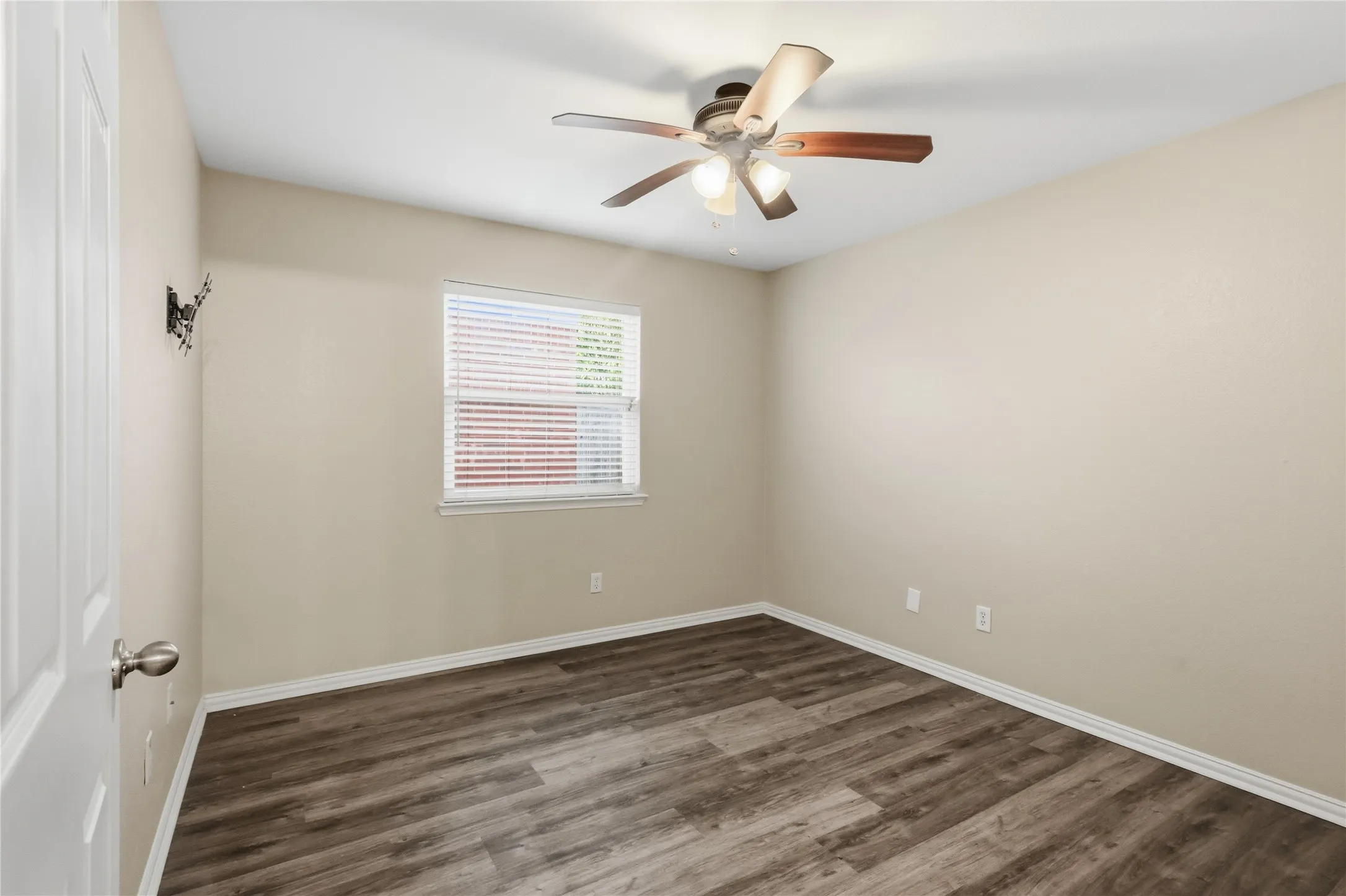 Neutral interior room featuring wood-finish flooring, a ceiling fan with integrated lighting, and a single-pane window with horizontal blinds