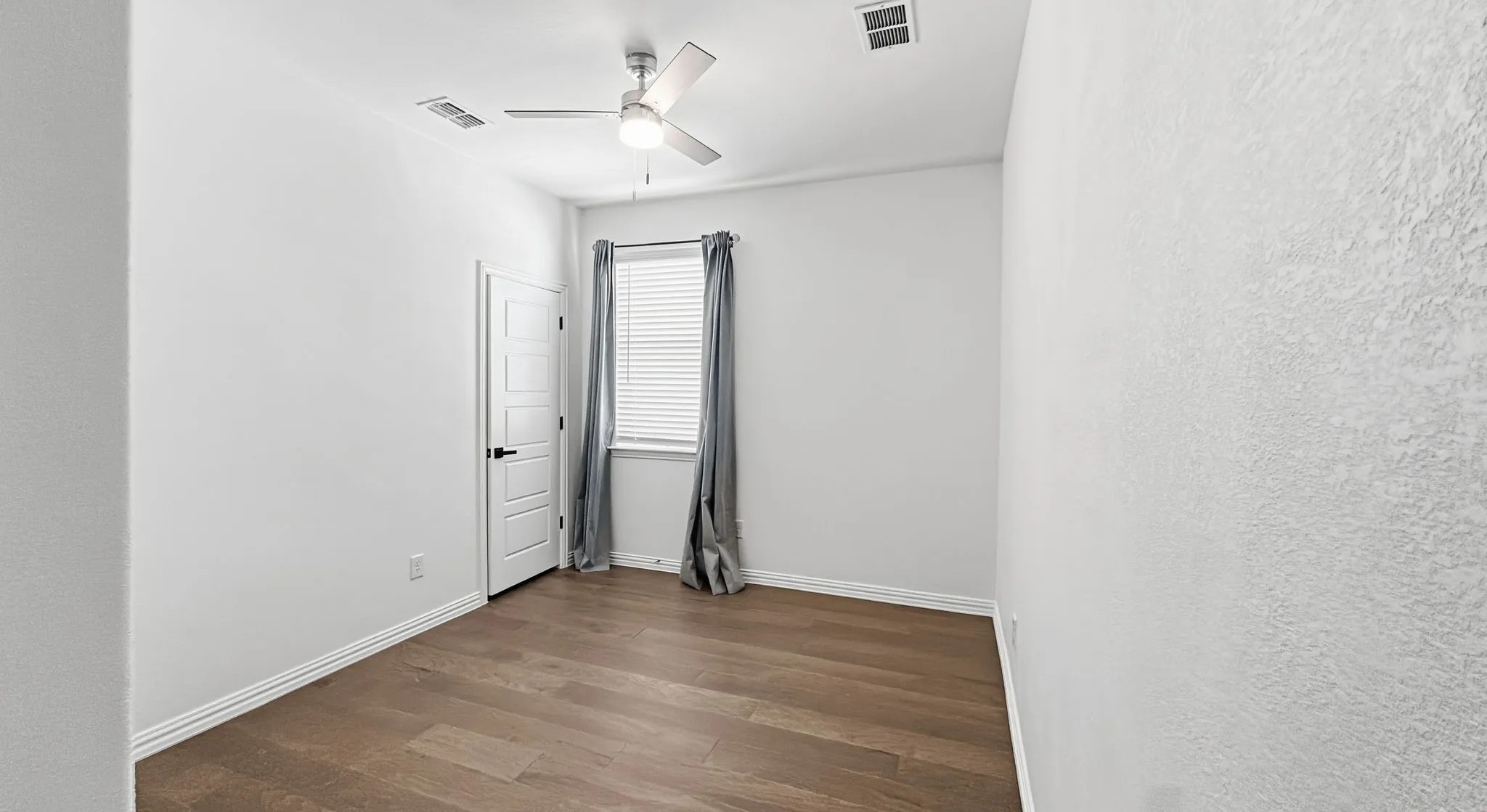 Interior room featuring wood-finish flooring, a neutral color palette, a ceiling fan with integrated lighting, and a multi-panel door with matte black hardware