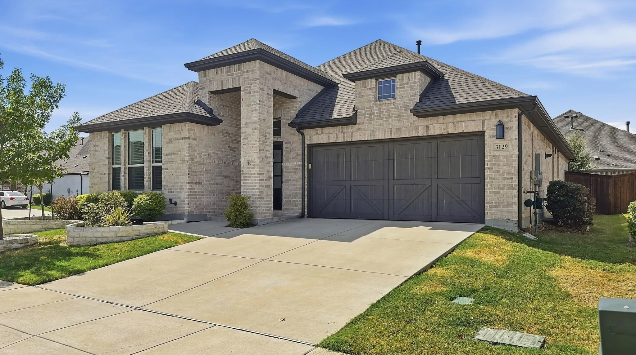 Brick exterior featuring a multi-gabled roofline, oversized two-car garage with decorative cross-buck detailing, and stone-bordered landscaping