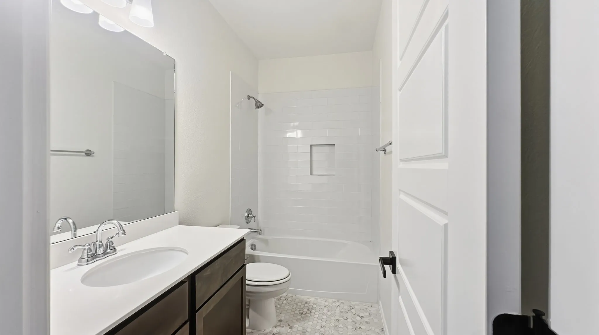 Bathroom featuring a dark-finish vanity with a white countertop, large wall-mounted mirror, tub-shower combination with white subway tile surround and integrated wall niche, and mosaic tile flooring