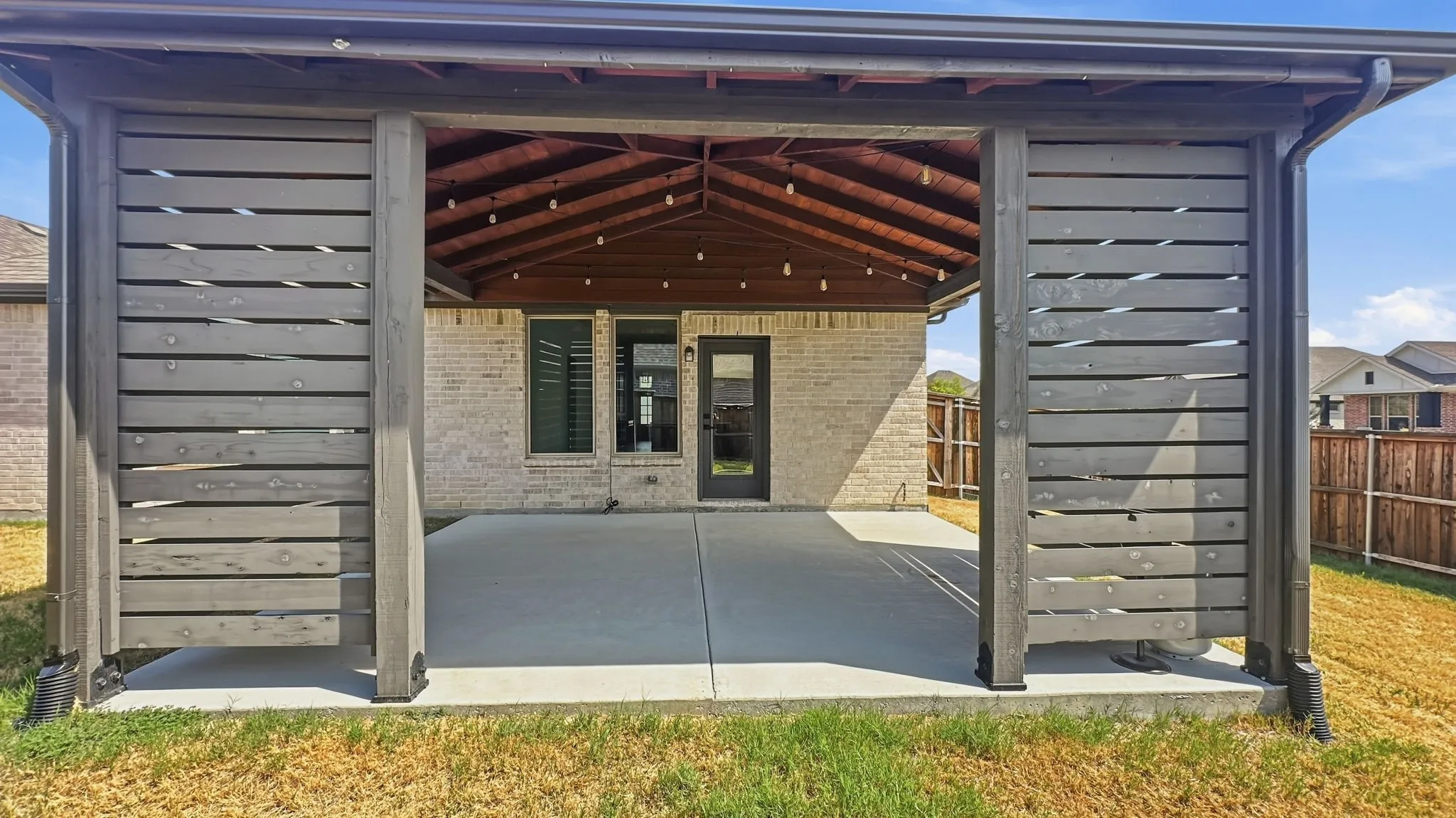 Covered patio featuring a wood-planked vaulted ceiling, horizontal wood privacy screening, and a concrete slab foundation