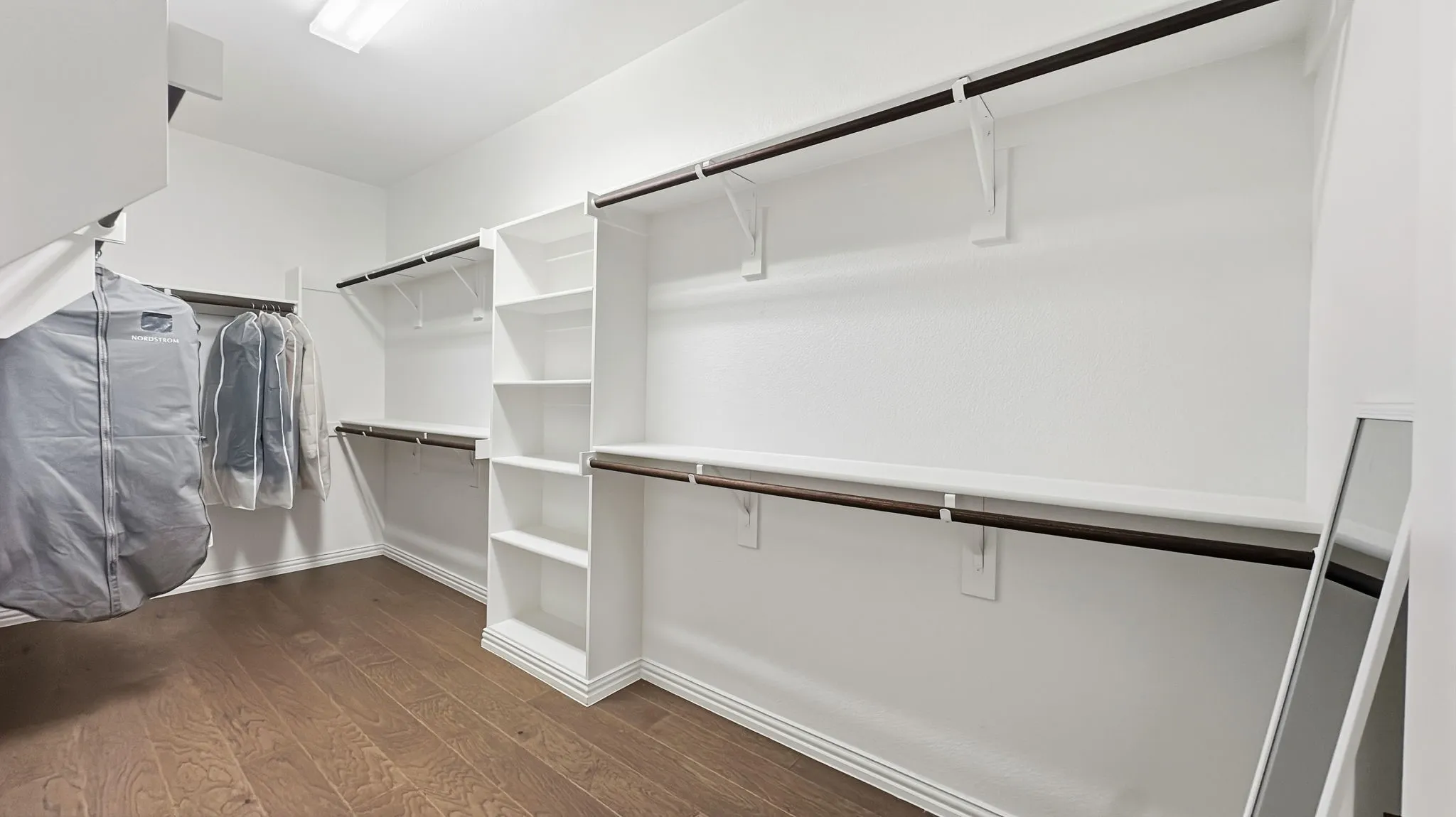 Walk-in closet featuring white built-in shelving, multi-level hanging rods, and wood-finish flooring