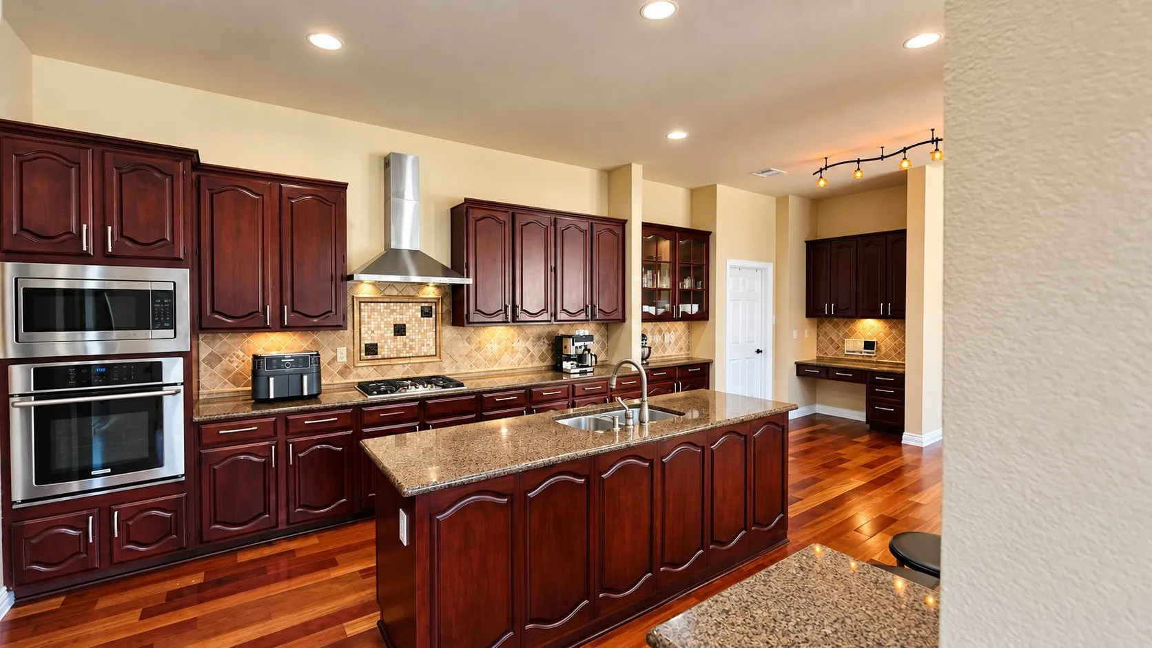 Kitchen featuring wood-finish flooring, dark wood cabinetry, stainless steel appliances, a center island with a sink, and recessed lighting