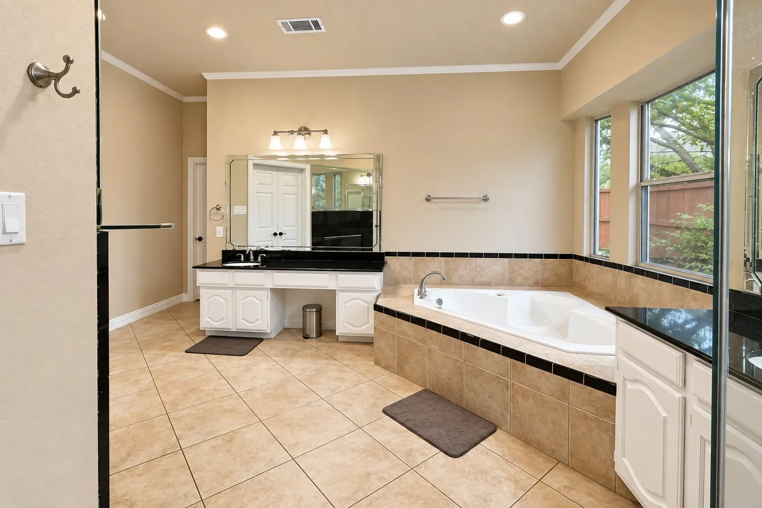 Corner soaking tub with tiled surround, dual windows, and recessed lighting