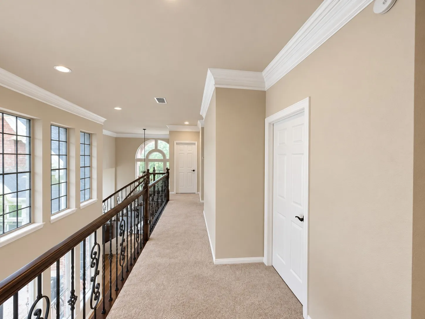 Upper-level hallway featuring a decorative wrought iron railing, arched window, recessed lighting, and crown molding