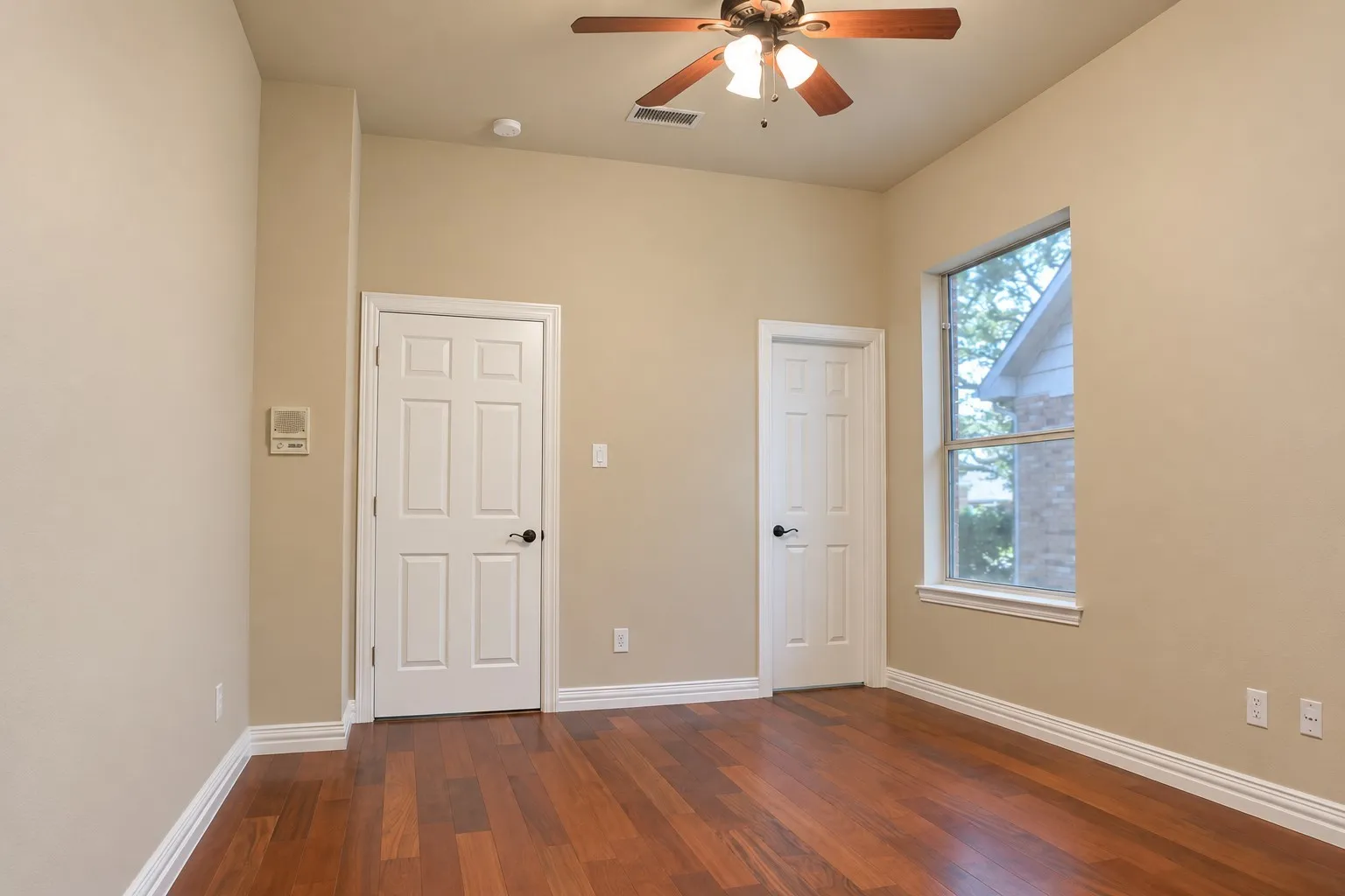 Wood-finish flooring, ceiling fan with integrated lighting, window with white trim, two panel doors, and white baseboards