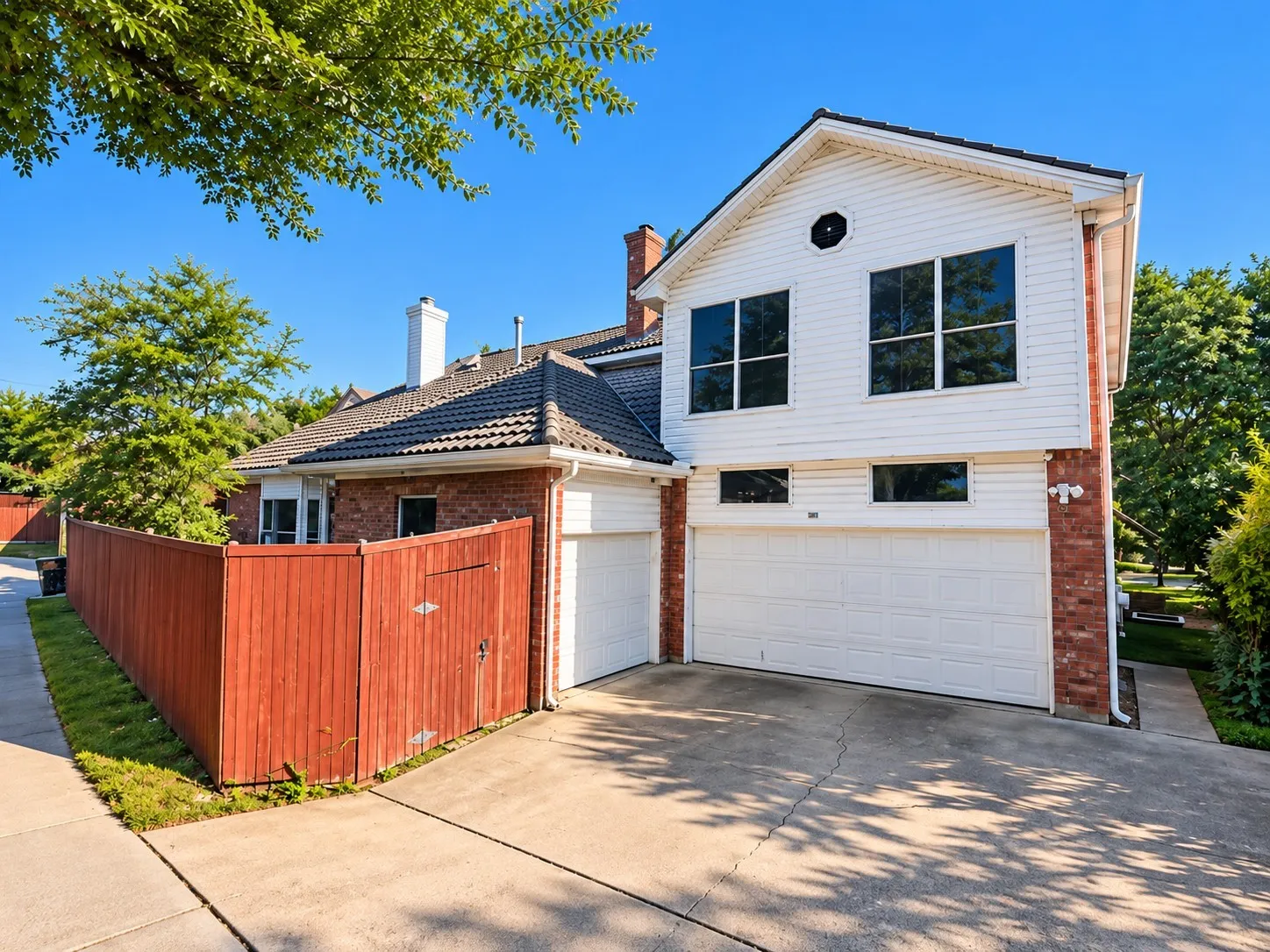 Brick and siding exterior with a two-car garage, mature trees, and a privacy fence